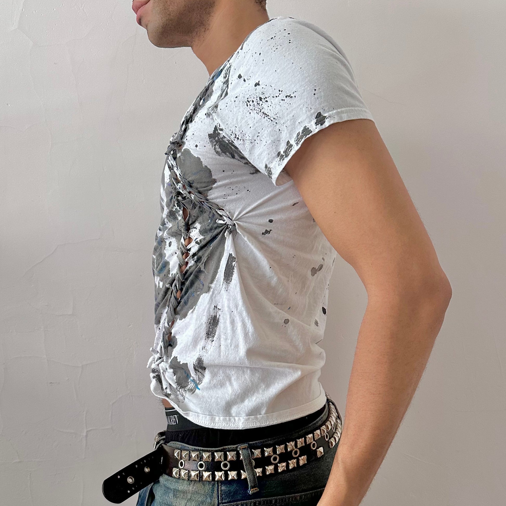 Left side detail of ASTROBOI* x Gildan 'Hidden Messages' showing hand-painted blue scribbles, watercolor ink splatters, and front braid detailing on white graphic tee.