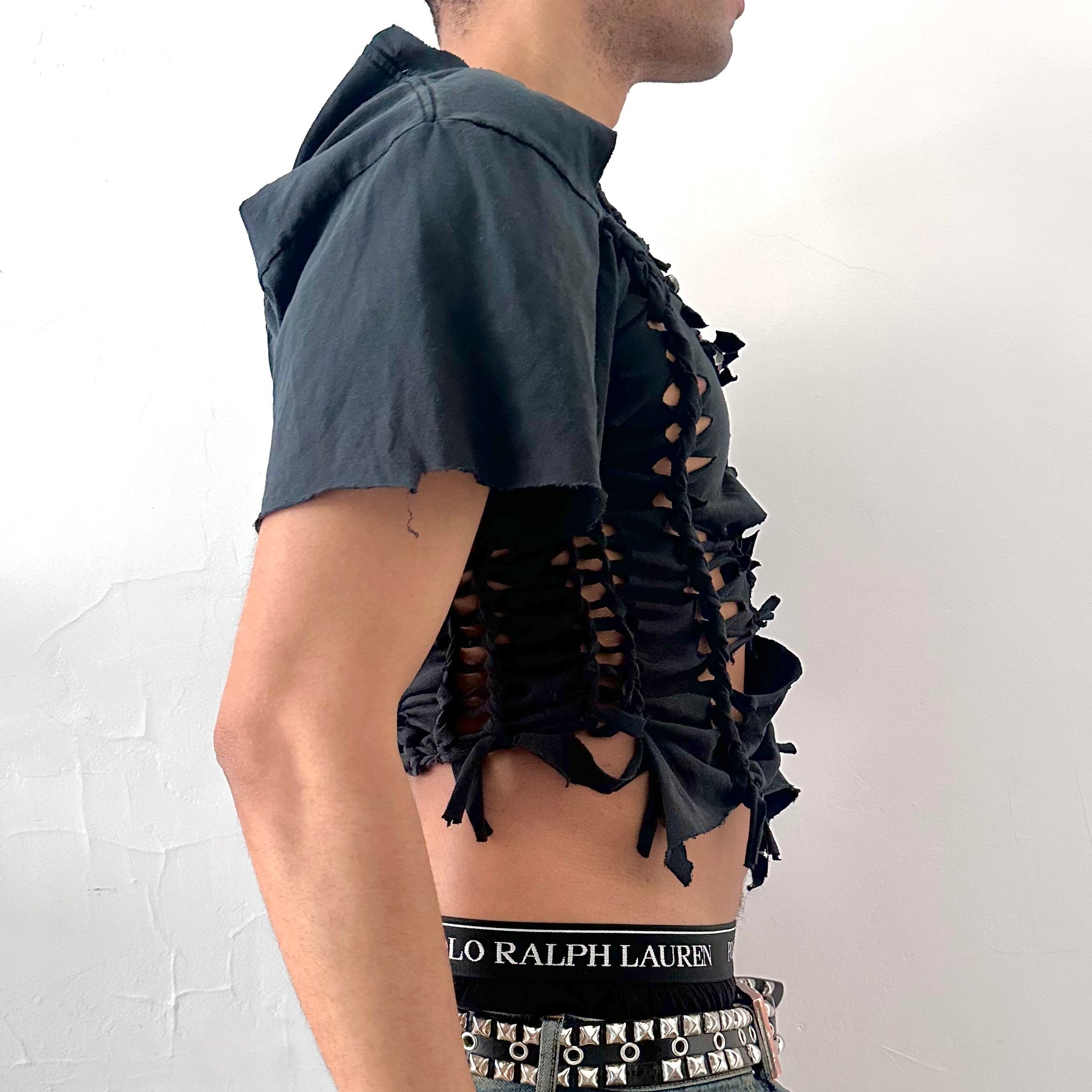 Right side detail of ASTROBOI* x Alpinestars tee showing asymmetric sleeve, braided construction, and ripped detailing on black base.