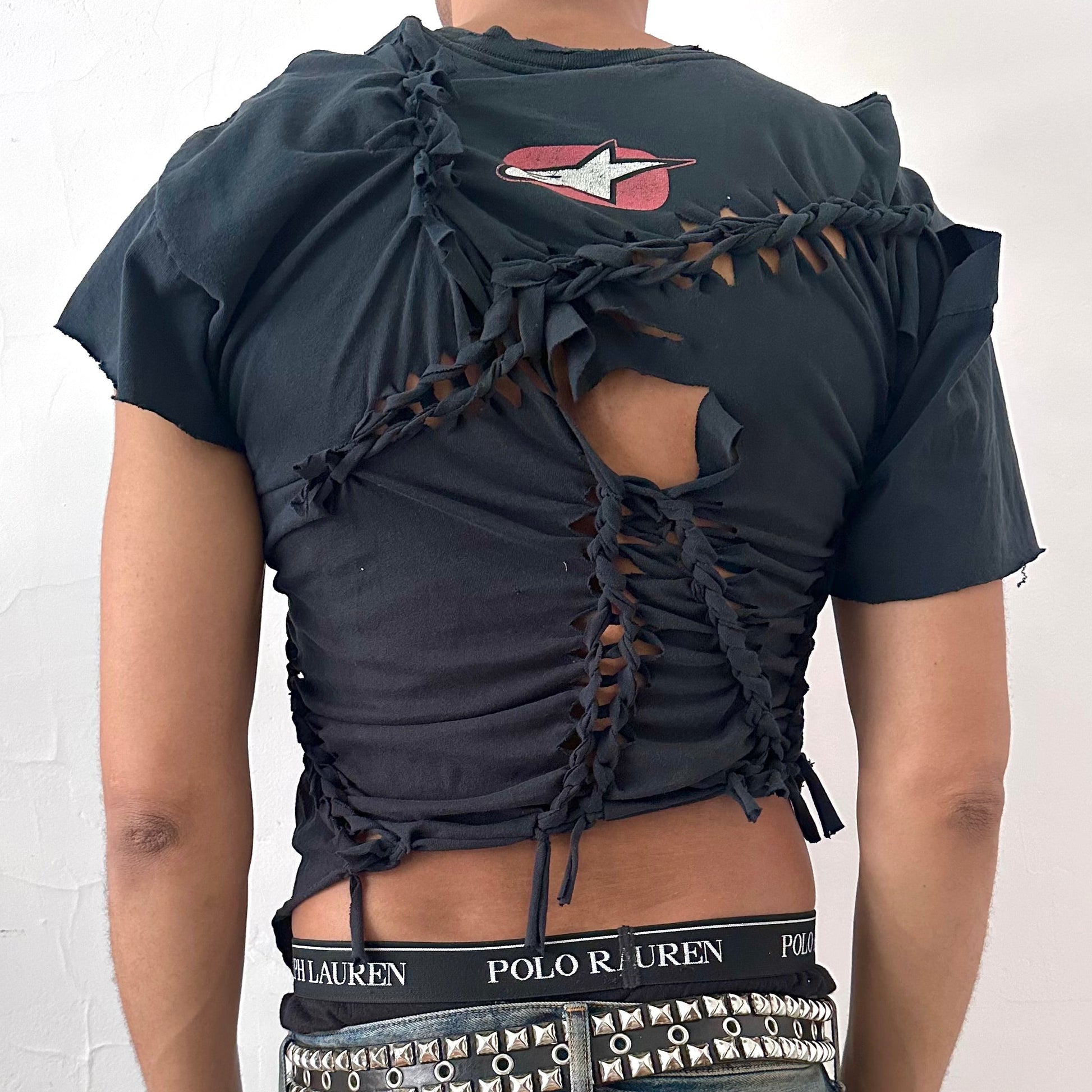 ASTROBOI* x Alpinestars black braided cut-out t-shirt, rear view showing Alpinestars back neck logo, asymmetric sleeves, and uneven hem, worn by male model.