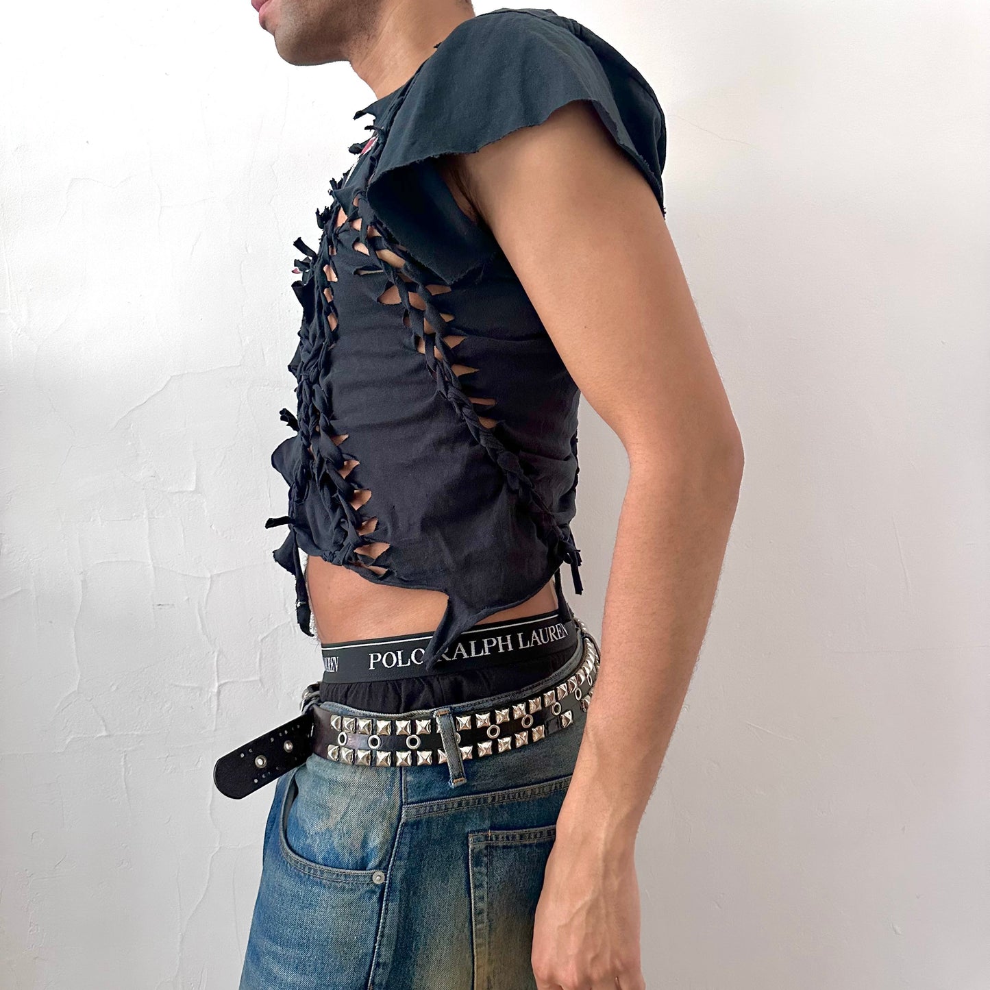 Left side detail of ASTROBOI* x Alpinestars tee showing asymmetric sleeve, uneven hem, and hand-braided ripped detailing on black deconstructed tee.