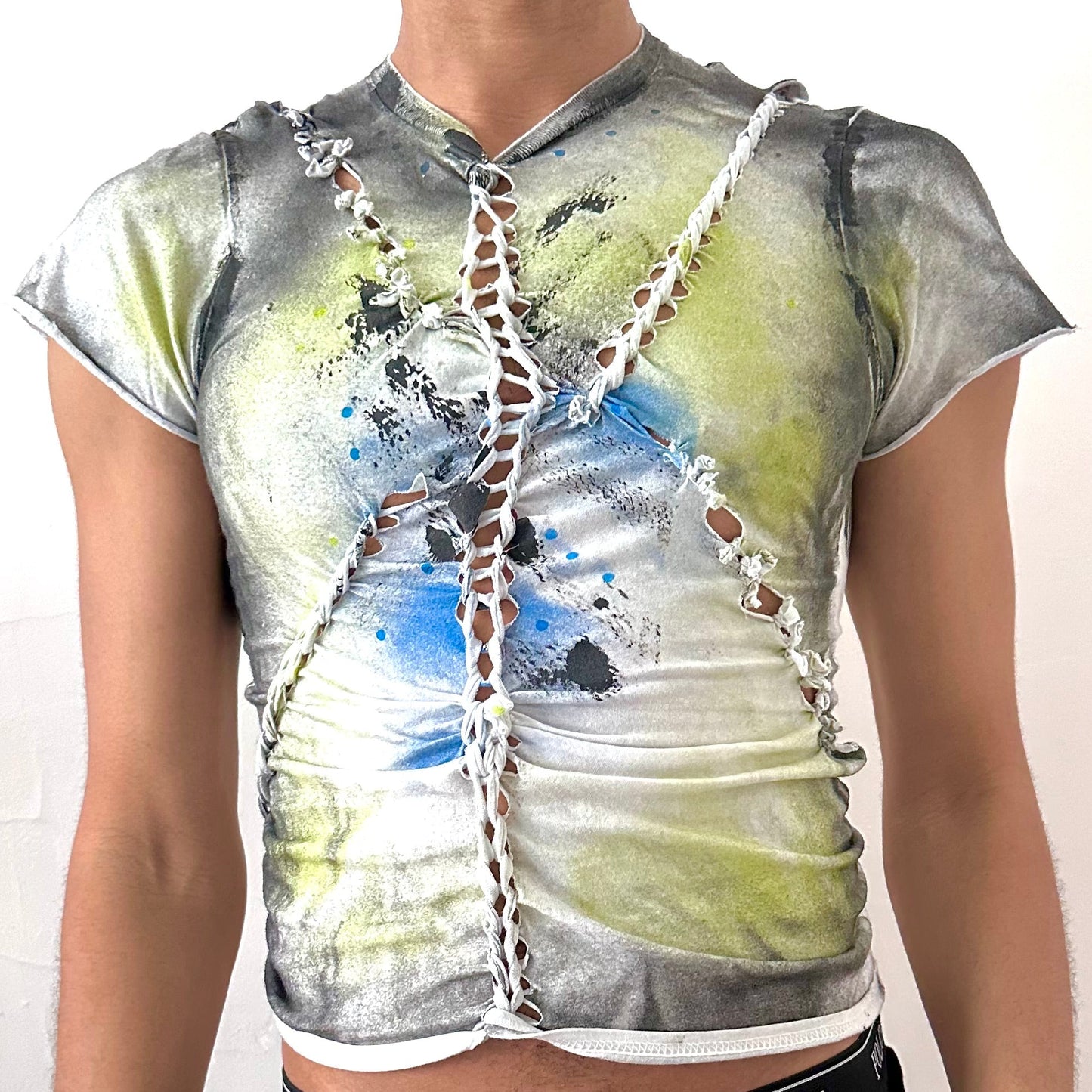 Close-up of ASTROBOI* x Gildan 'Algae' showing hand-braided construction and acid green, black, and blue abstract print on heavyweight white cotton fabric.