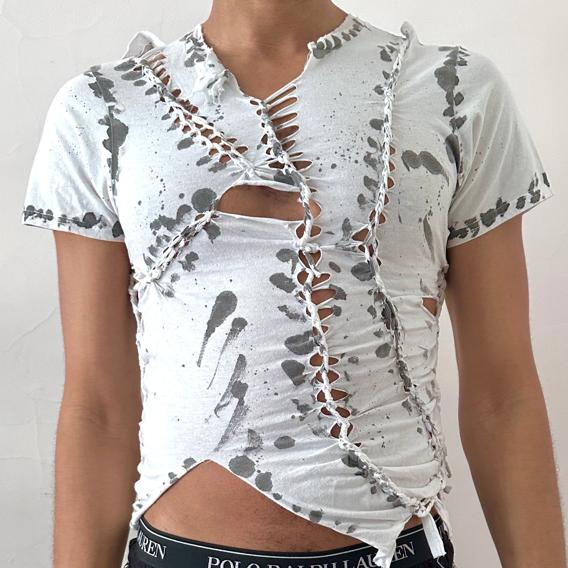 Close-up of ASTROBOI* x Gildan '1001' showing hand-braided construction, cut-out detailing, and bold black painted pattern on white cotton fabric.
