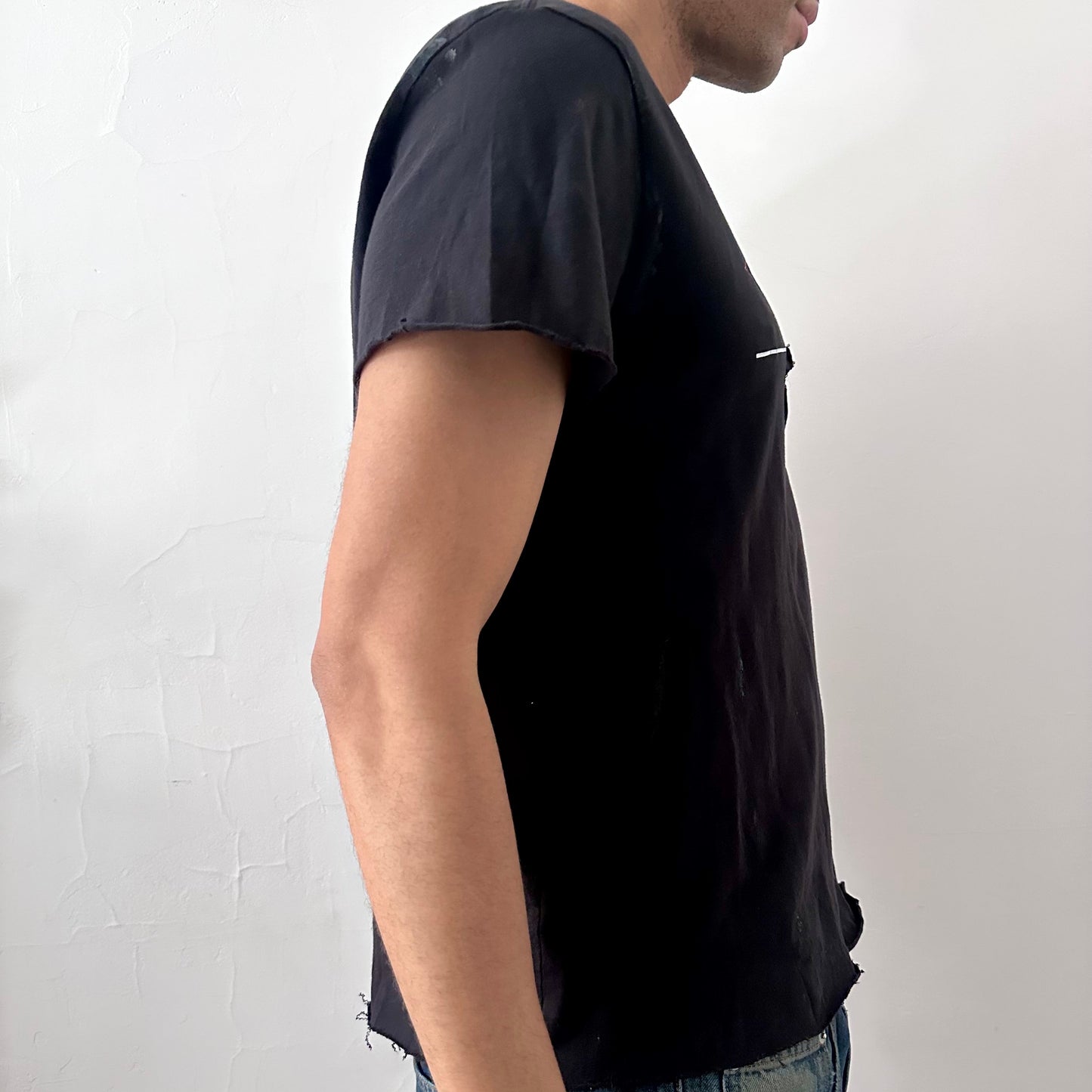 Right side detail of ASTROBOI* x CK Jeans tee showing asymmetric sleeve construction and uneven hem on loose-fitting black base.