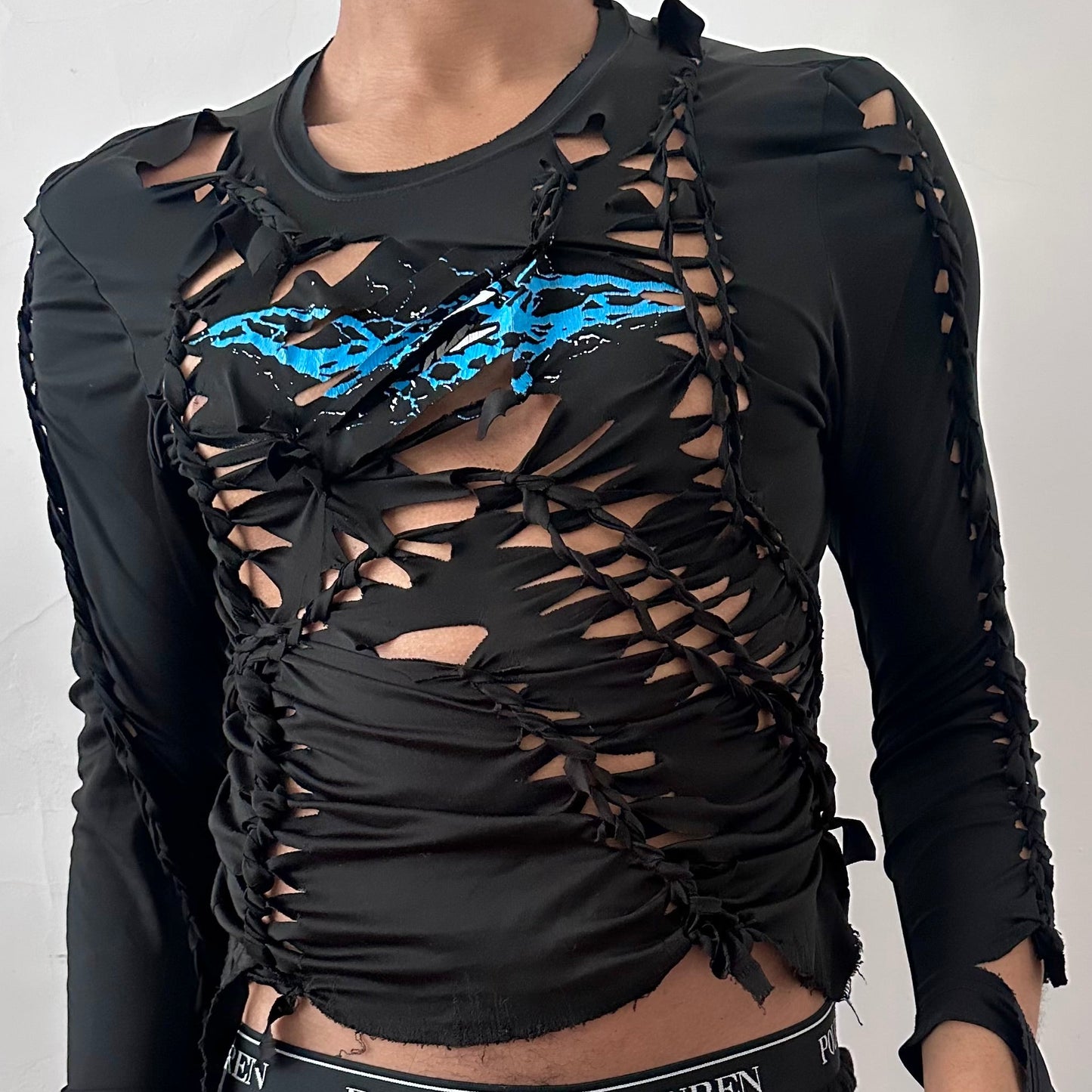 Close-up of ASTROBOI* 'Thunder' showing blue and white lightning graphic at center chest, hand-braided construction, and cut-out detailing on black stretch Lycra fabric.