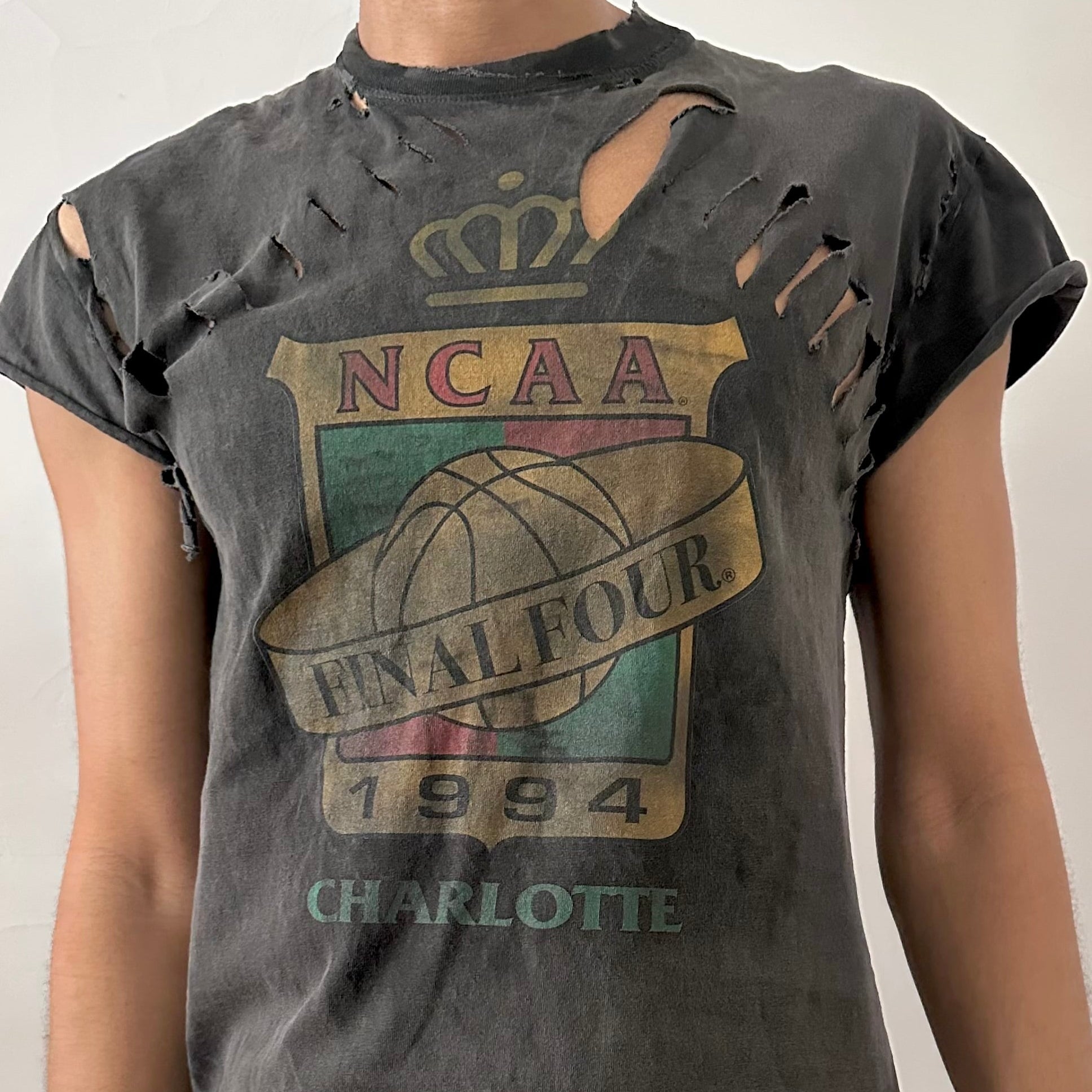 Close-up of ASTROBOI* NCAA Basketball tank showing muted chest graphic, distressed holes, and raw edge detailing on black cotton fabric.