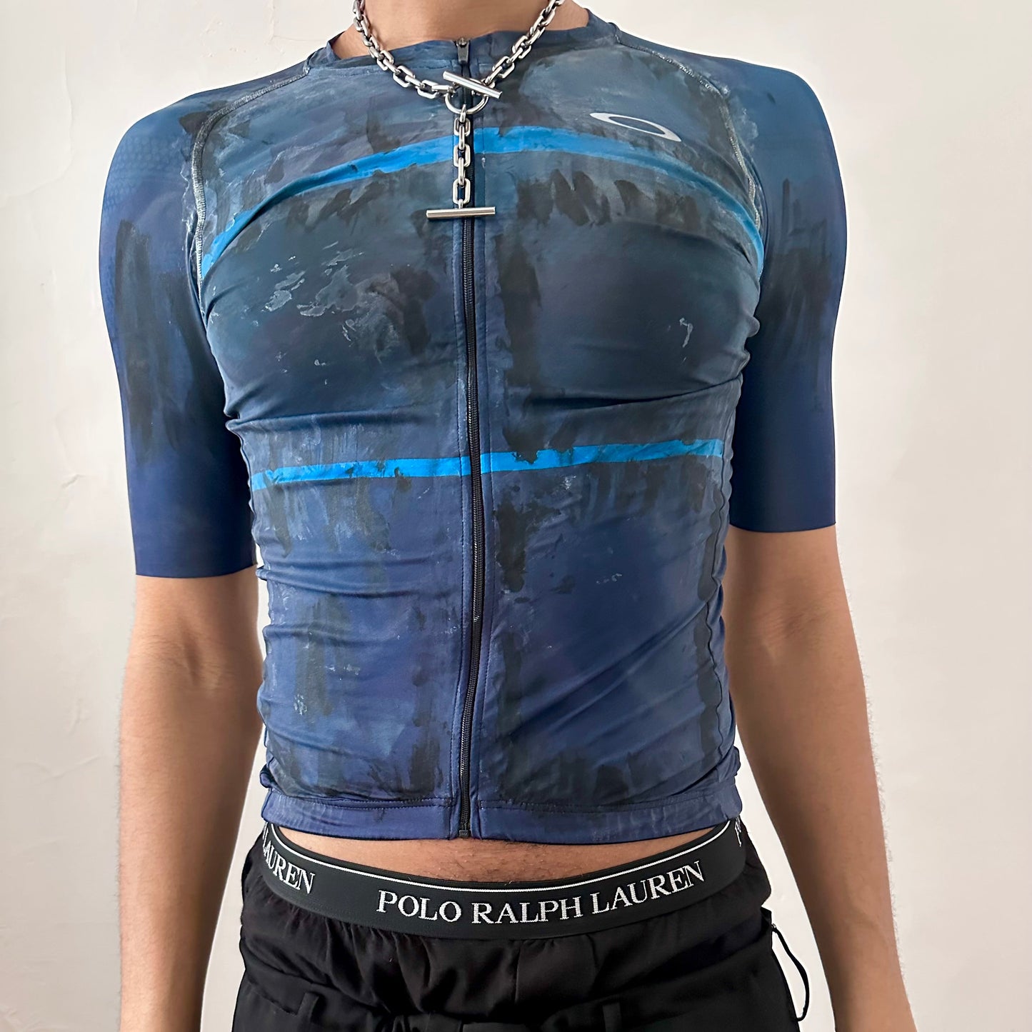 ASTROBOI* x Oakley blue painted cycling jersey with white and black painterly pattern, zipper closure, and Oakley logo at right chest, slim fitting, front view.