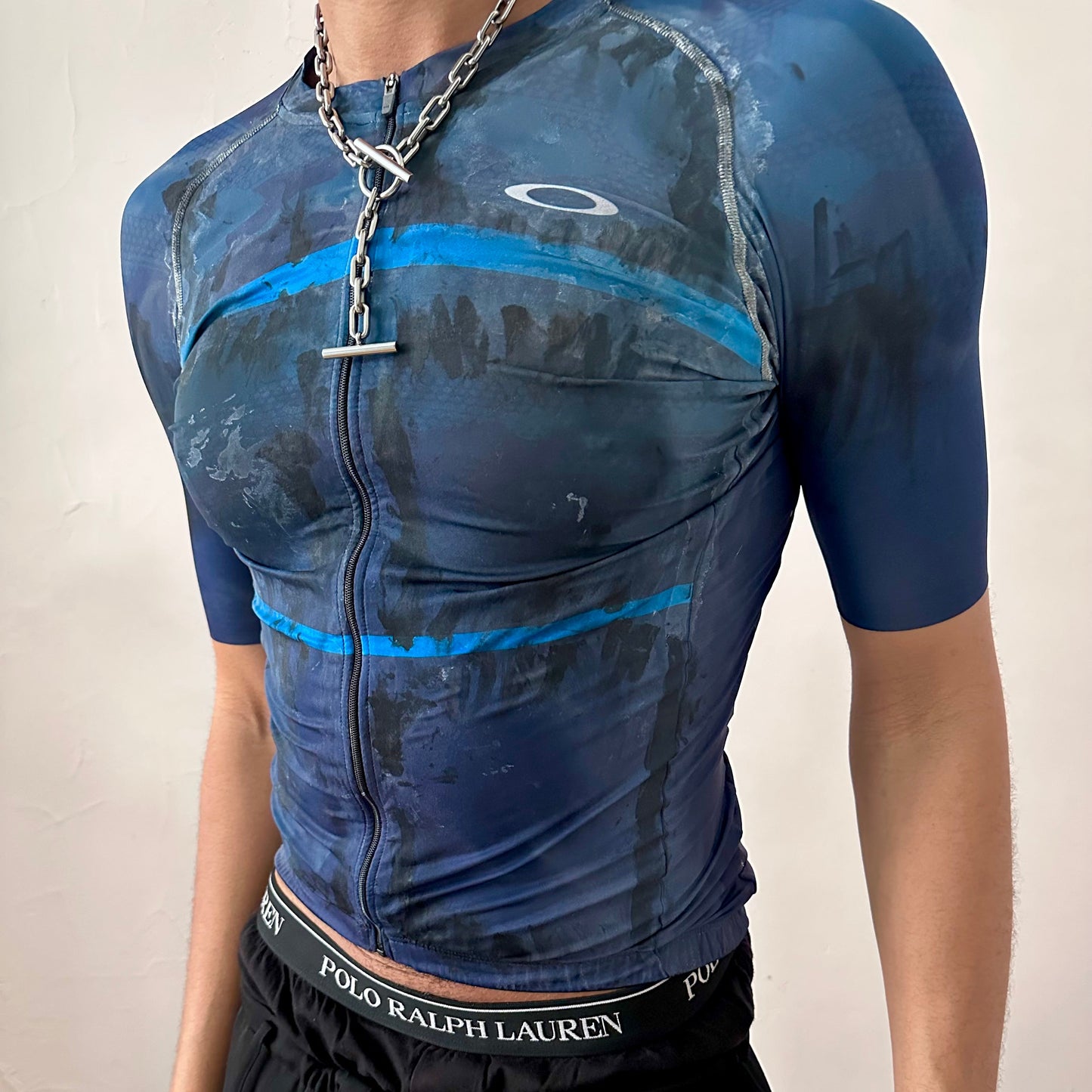 Close-up of ASTROBOI* x Oakley cycling jersey showing white and black painterly pattern detail and Oakley logo on blue and black base fabric.