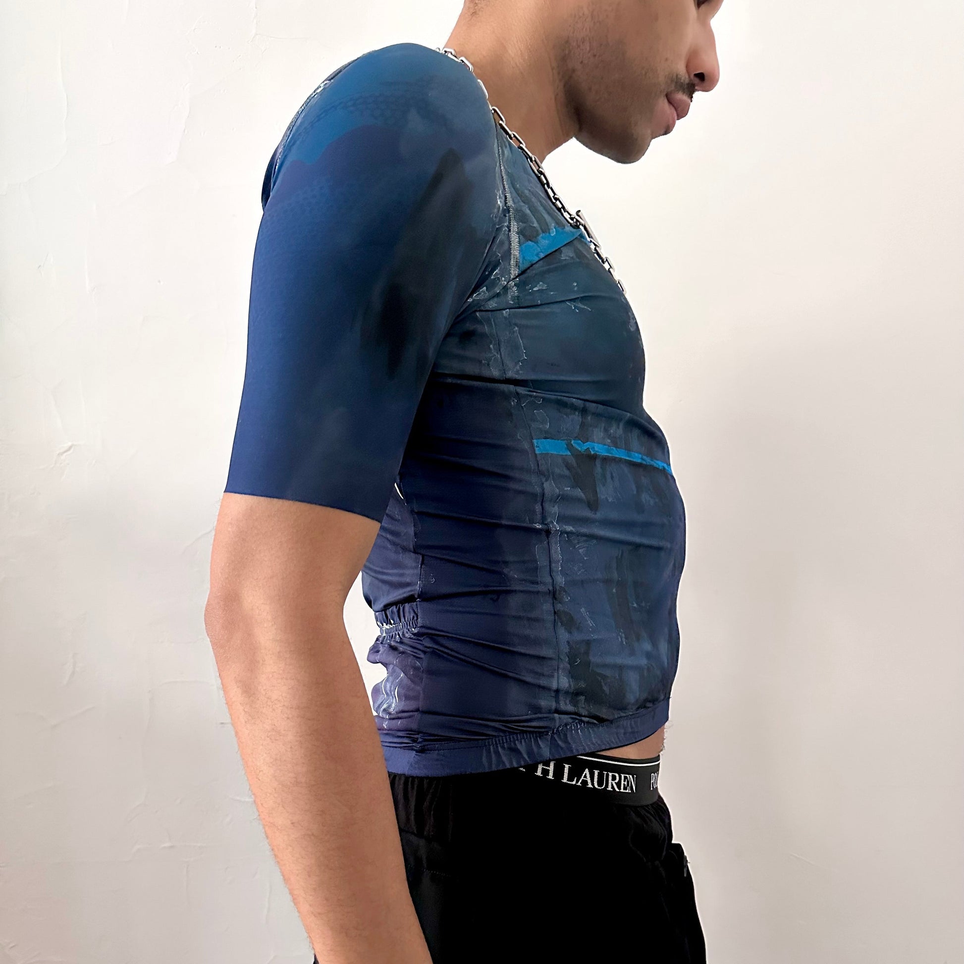 Right side detail of ASTROBOI* x Oakley cycling jersey showing white and black painterly pattern and Oakley logo on slim-fitting blue and black base.