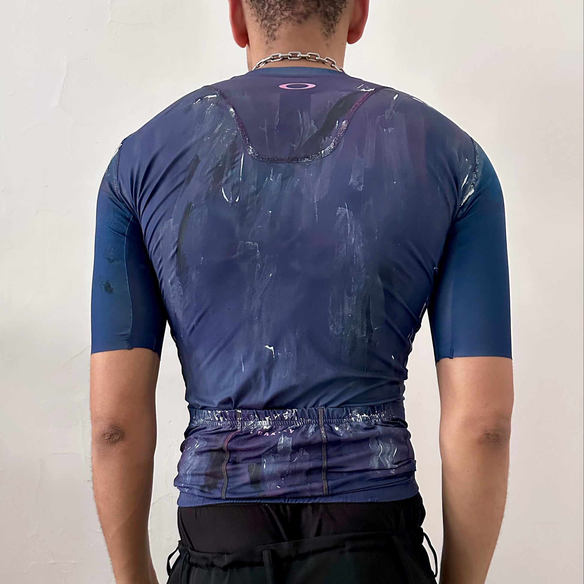 ASTROBOI* x Oakley blue painted cycling jersey, rear view showing Oakley back logo, back pockets, and white and black painterly pattern, worn by male model.