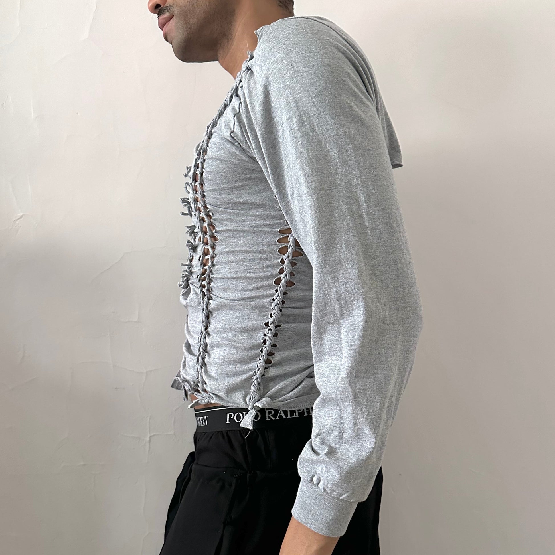 Left side detail of ASTROBOI* x Gildan 'Neutral' showing hand-braided arrangement, knot detail, and cut-outs on cropped gray long sleeve.