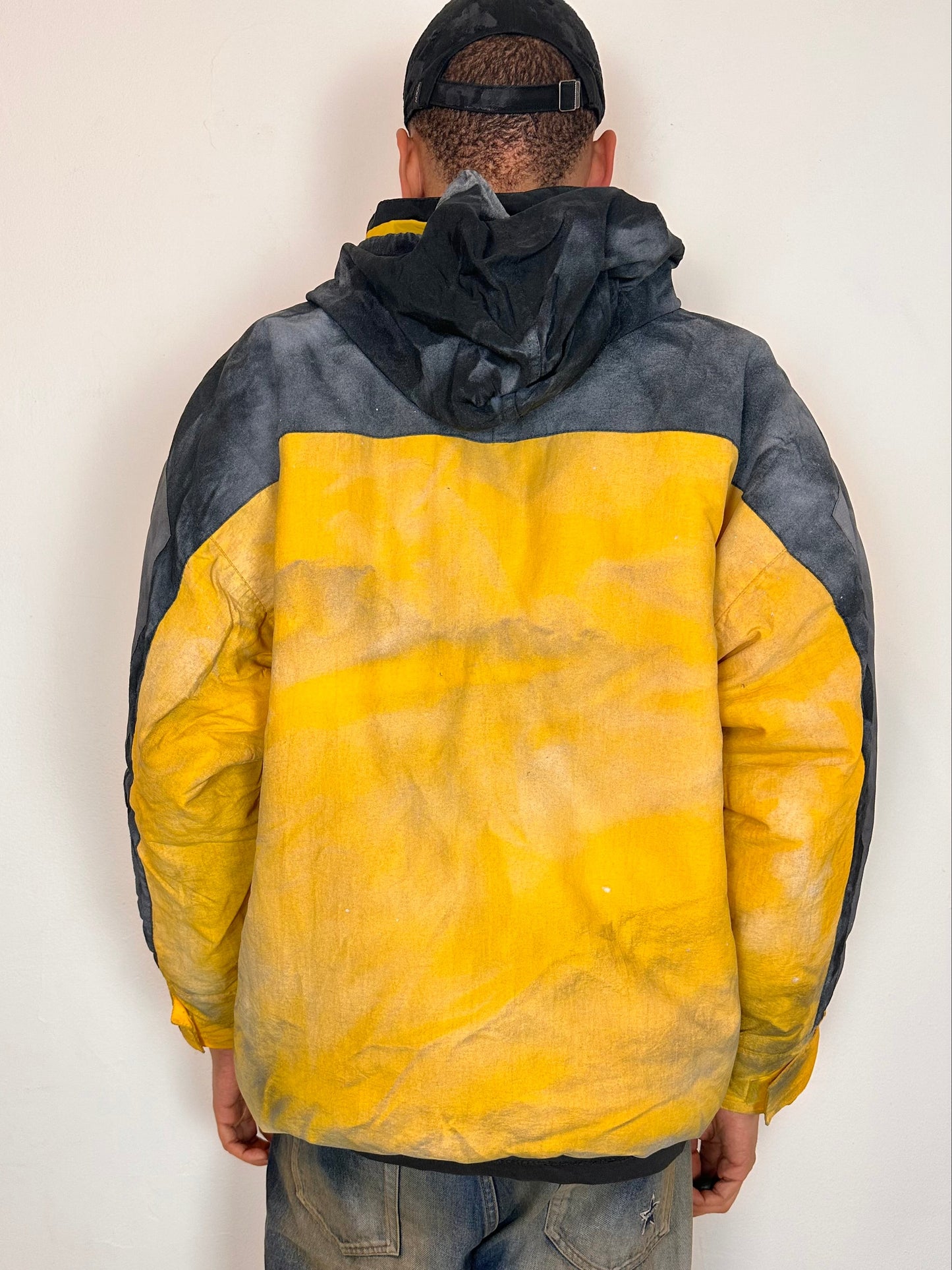 Back of ASTROBOI* x Starter yellow and black airbrushed puffer jacket with grey sleeves, reflective taping, and adjustable toggles, men’s XL.