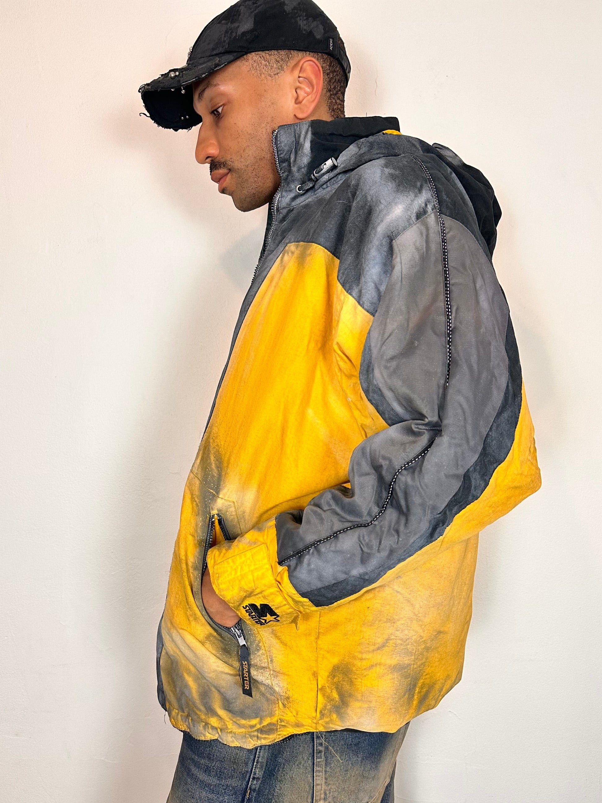 Left side of ASTROBOI* x Starter yellow and black airbrushed puffer jacket with grey sleeves, reflective taping, and adjustable toggles, men’s XL.