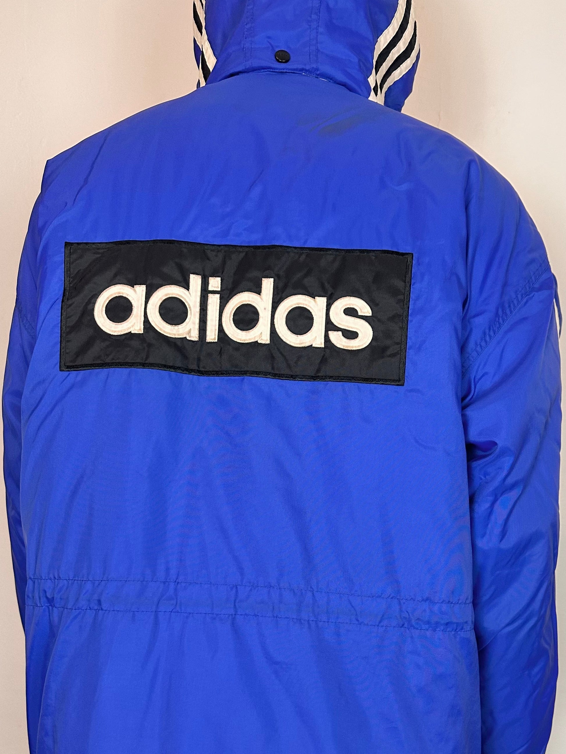 Back close up of Vintage Adidas blue oversized winter puffer coat with detachable hood, white stripes, and long insulated silhouette, size XXL.