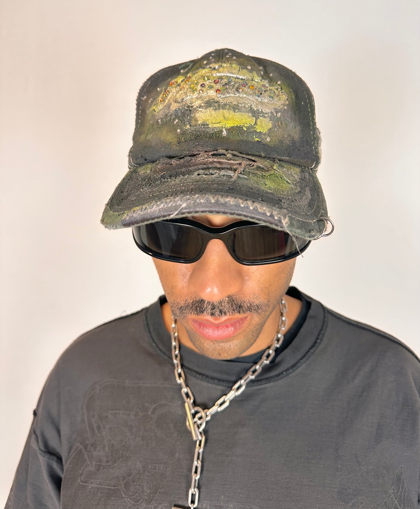 Front overview of “Green and brown distressed ASTROBOI* Hawaii hat with rhinestones, metallic paint, and sterling-steel piercings, customized in NYC.”