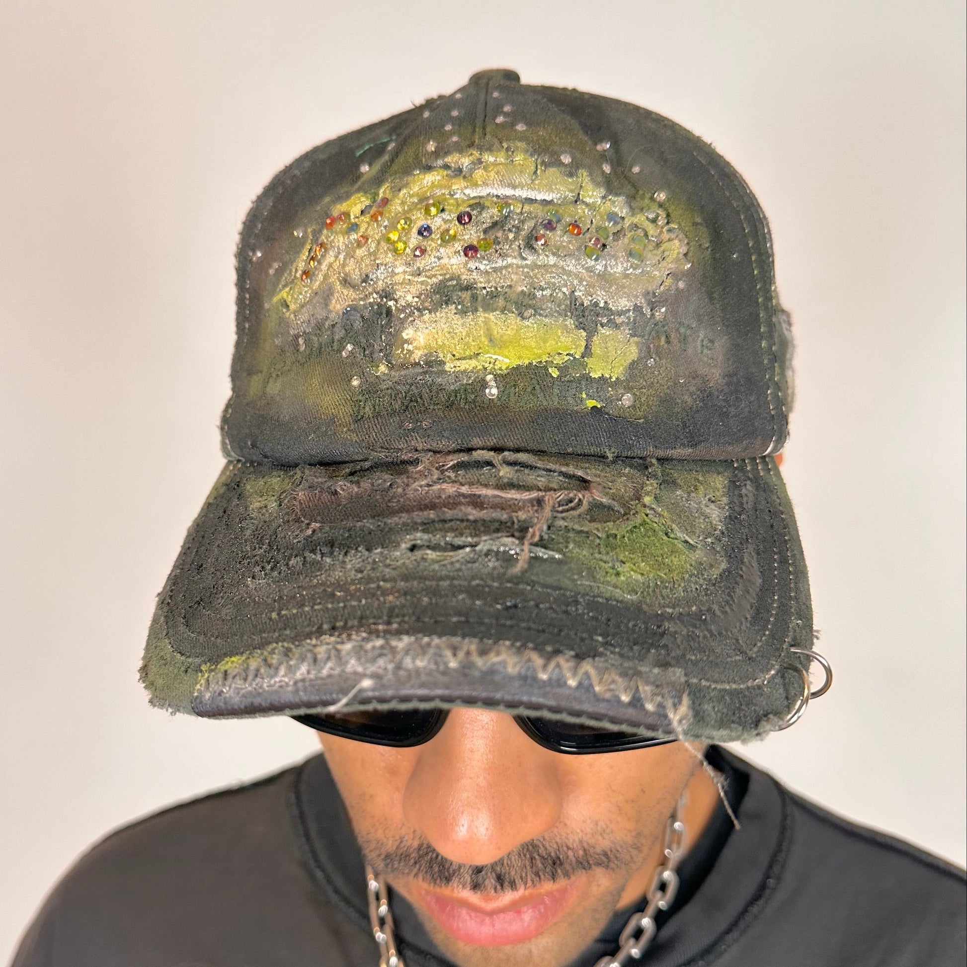 Front of of “Green and brown distressed ASTROBOI* Hawaii hat with rhinestones, metallic paint, and sterling-steel piercings, customized in NYC.”