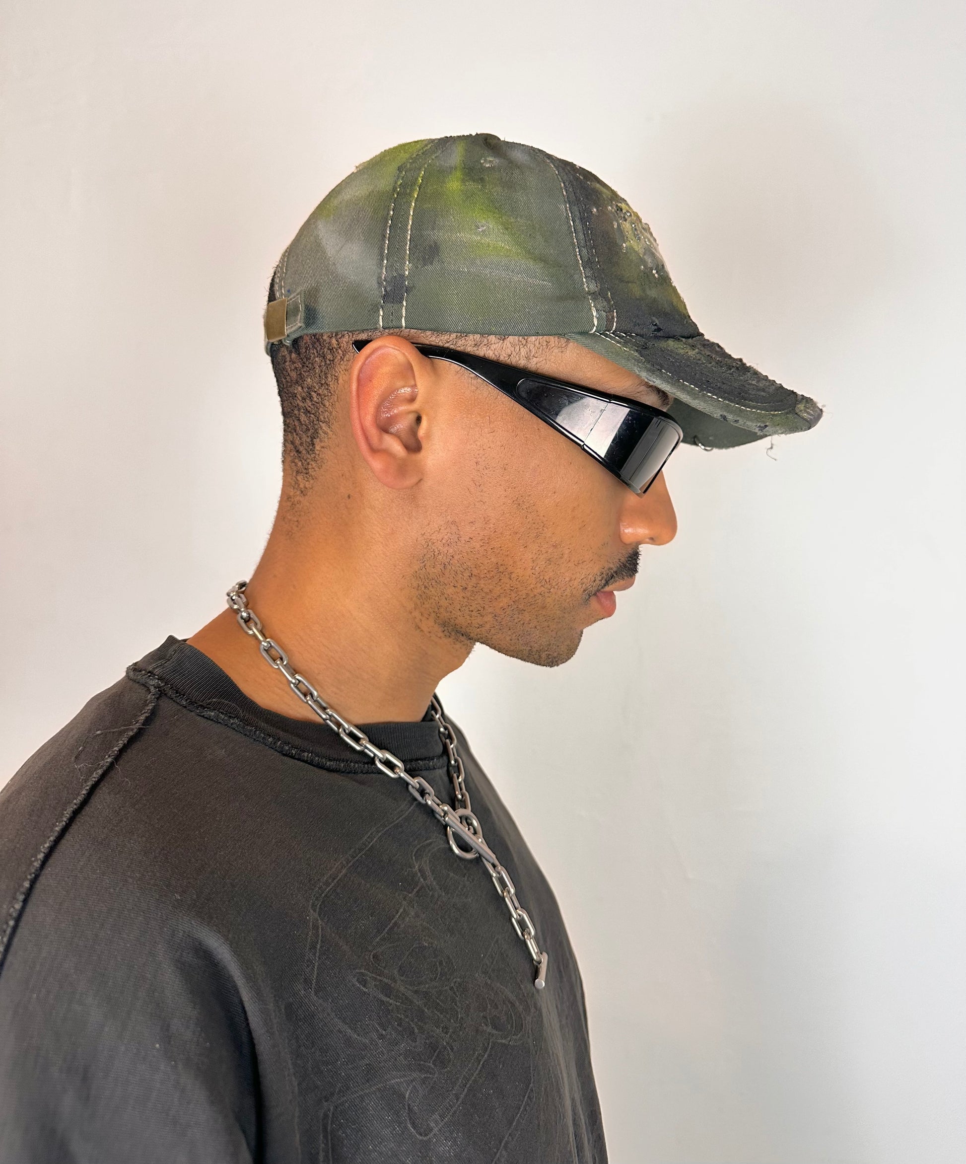 Right side of “Green and brown distressed ASTROBOI* Hawaii hat with rhinestones, metallic paint, and sterling-steel piercings, customized in NYC.”