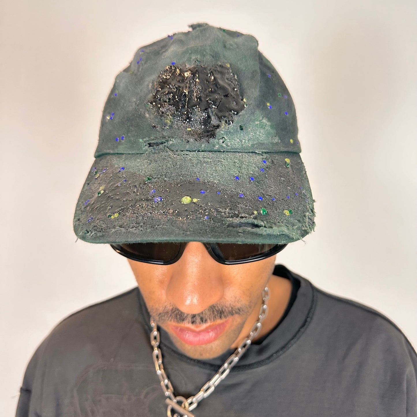 Front of ASTROBOI* green 818 baseball cap with blue rhinestones, black resin slime effect, airbrushed paint details, light distressing, and an adjustable back strap.