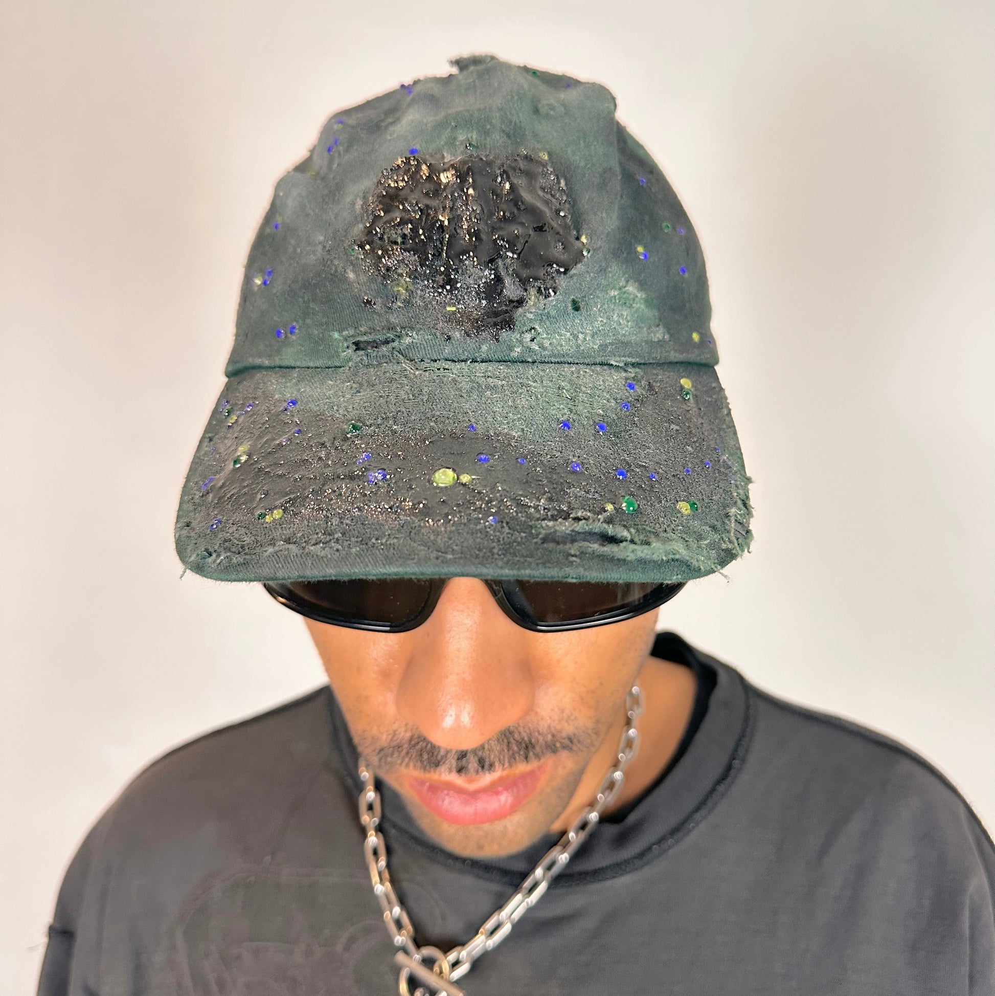 Front of ASTROBOI* green 818 baseball cap with blue rhinestones, black resin slime effect, airbrushed paint details, light distressing, and an adjustable back strap.