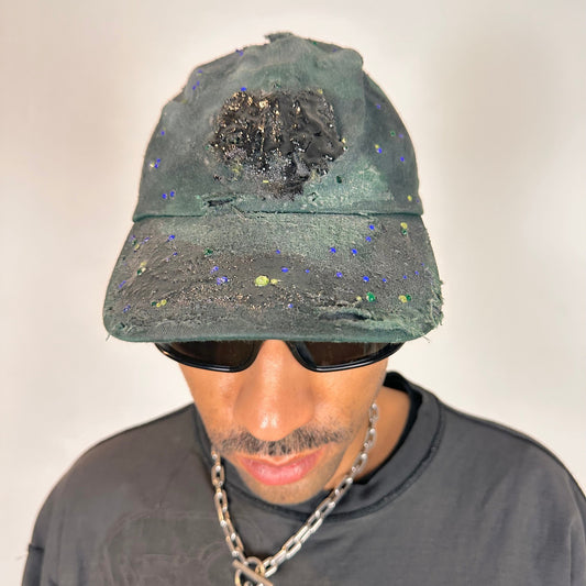 Front of ASTROBOI* green 818 baseball cap with blue rhinestones, black resin slime effect, airbrushed paint details, light distressing, and an adjustable back strap.