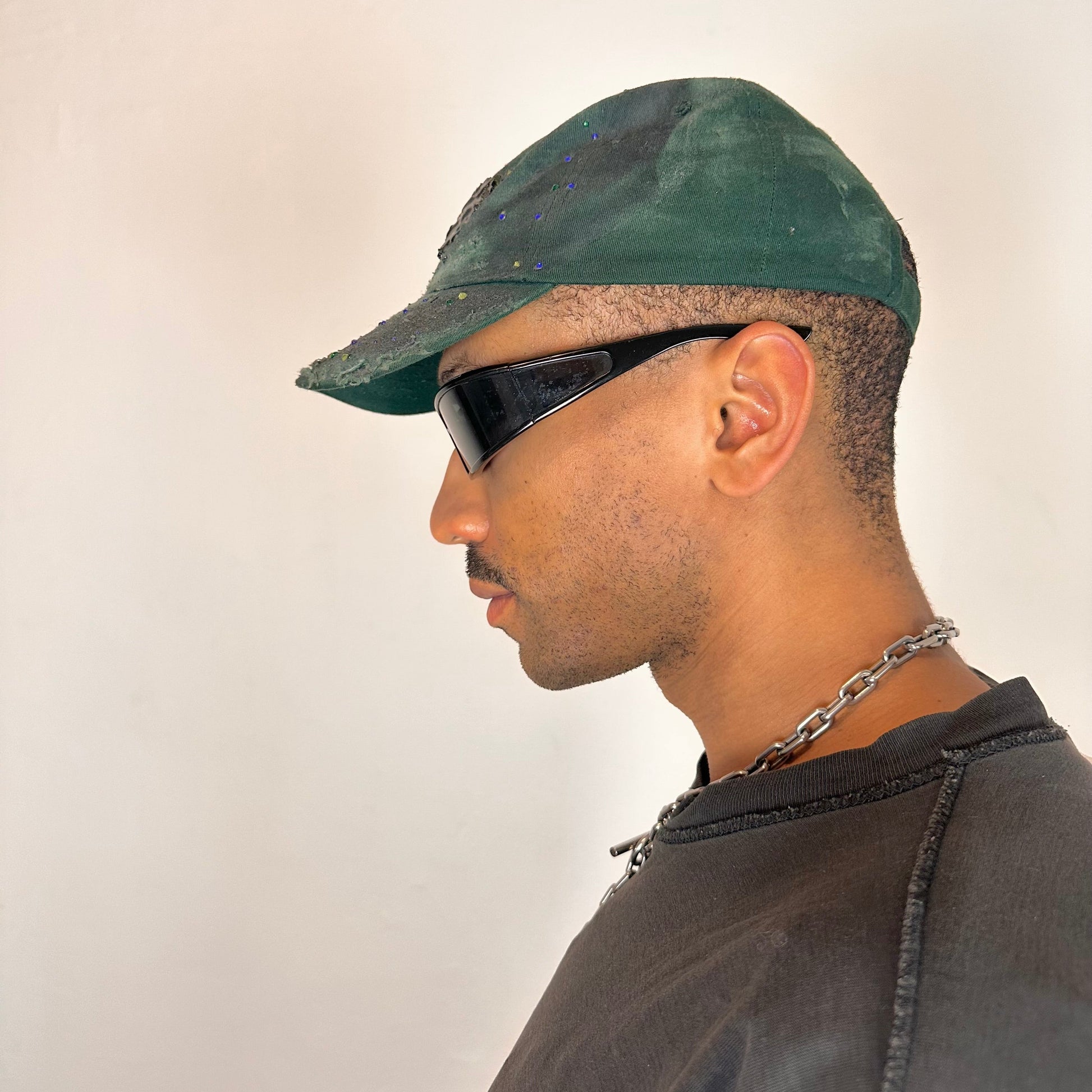 Left side of ASTROBOI* green 818 baseball cap with blue rhinestones, black resin slime effect, airbrushed paint details, light distressing, and an adjustable back strap.