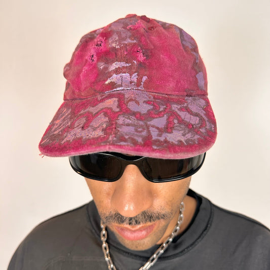 Front of ASTROBOI* MARS distressed metallic cap with lavender paint accents, bent visor, and safety pin adjustment detail.