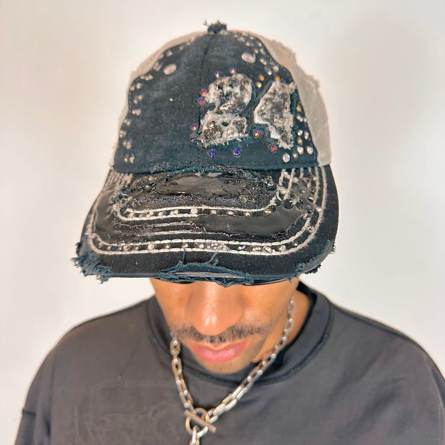 Front of ASTROBOI* “24” black racing cap with silver rhinestones, white stitching, glossy black resin details, and adjustable Velcro back closure.