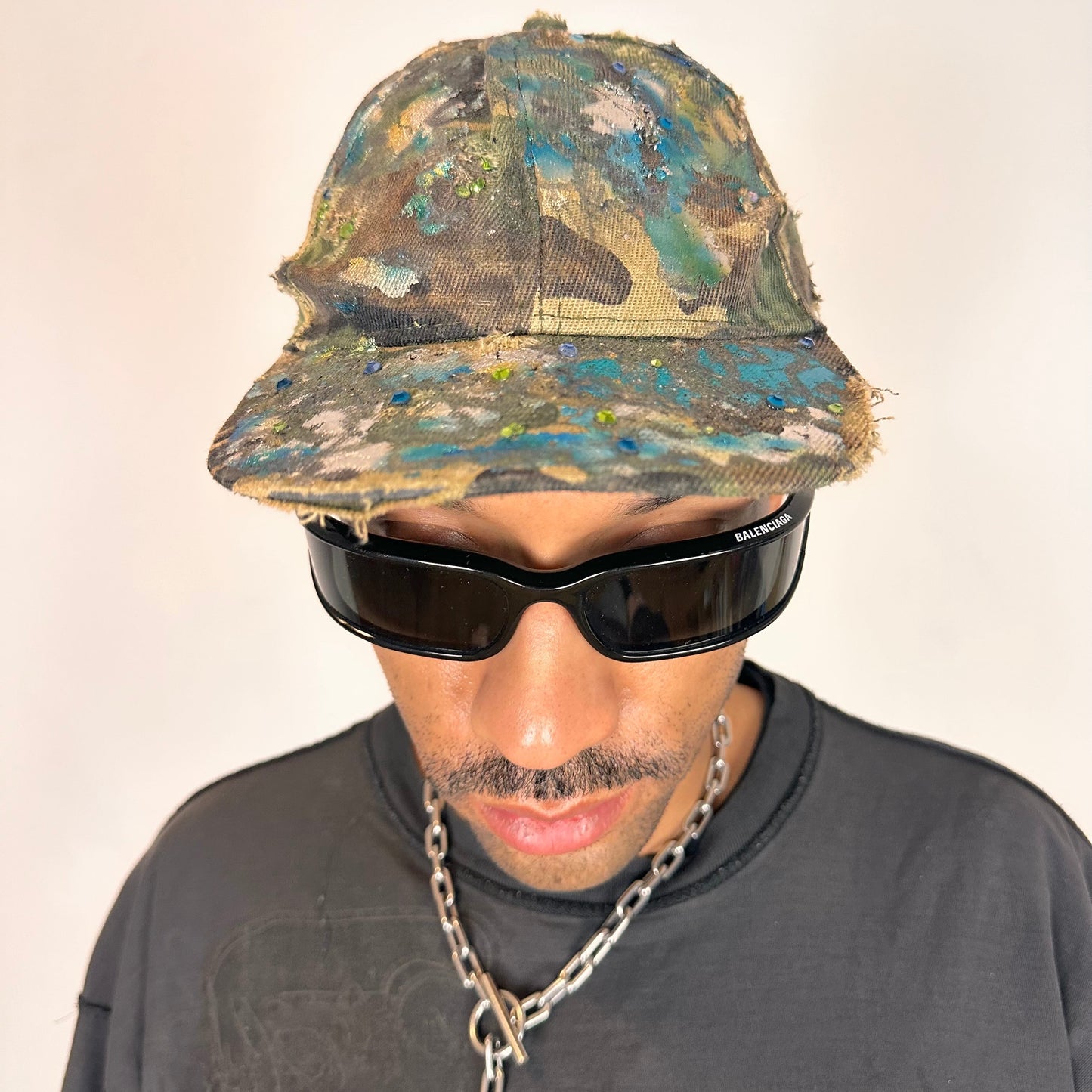 Overview of ASTROBOI* distressed brown camouflage cap with metallic silver and blue paint and tonal rhinestone accents, adjustable velcro back.