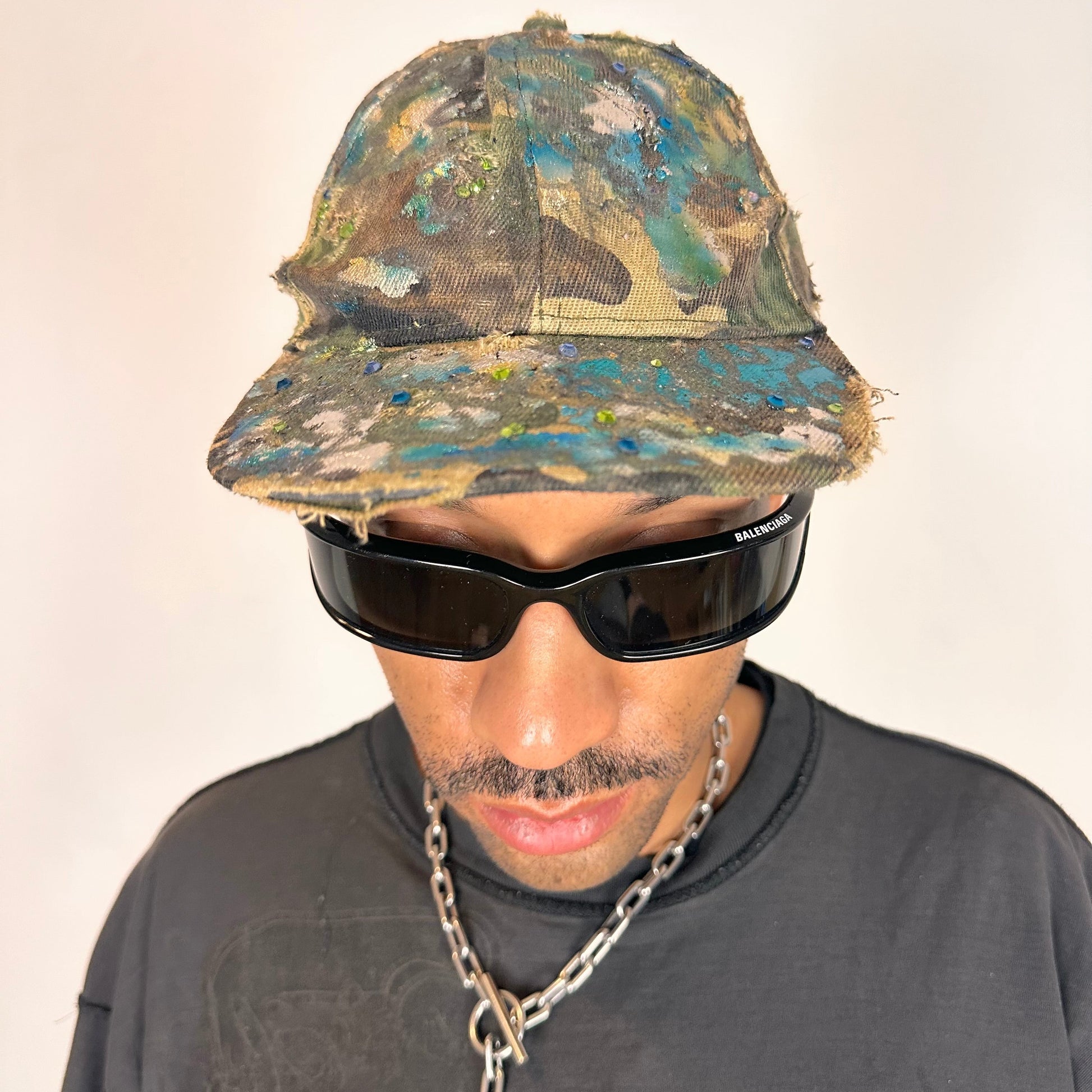 Overview of ASTROBOI* distressed brown camouflage cap with metallic silver and blue paint and tonal rhinestone accents, adjustable velcro back.