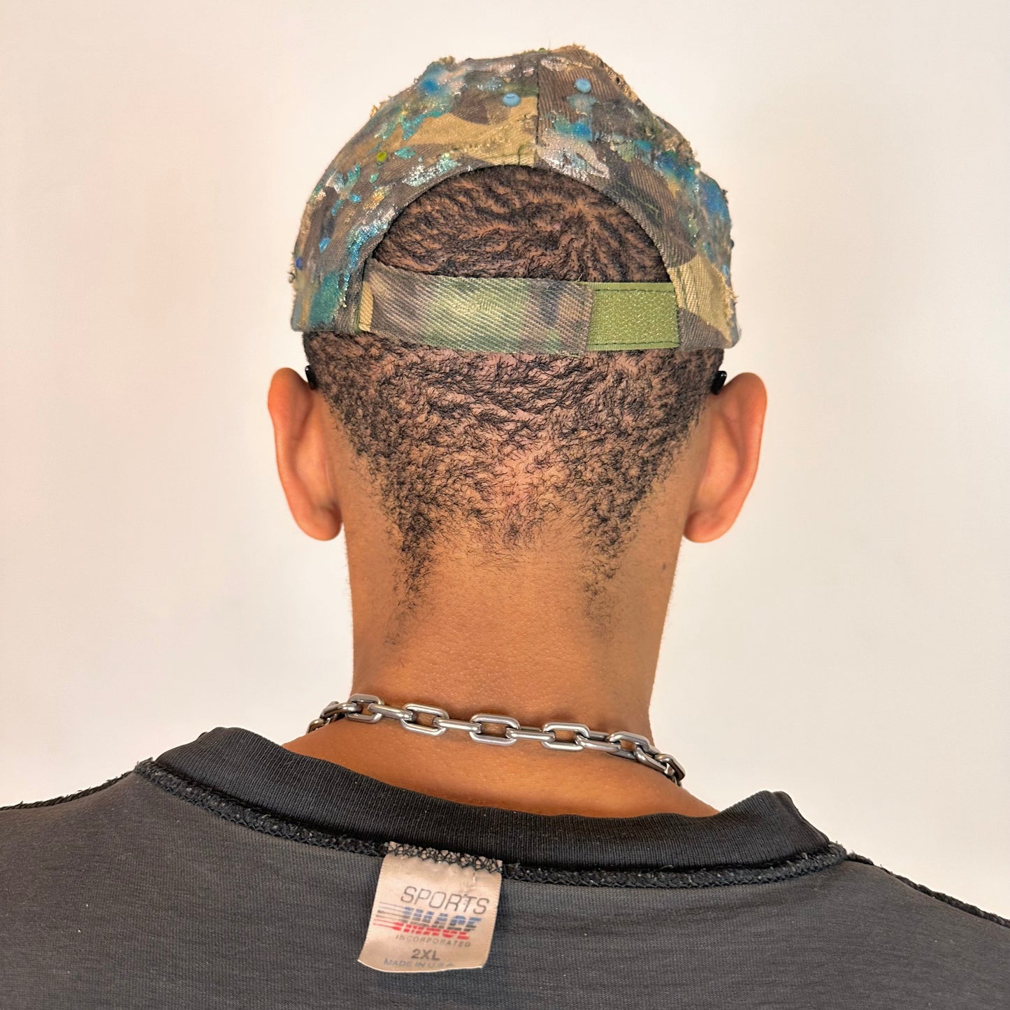 Back of ASTROBOI* distressed brown camouflage cap with metallic silver and blue paint and tonal rhinestone accents, adjustable velcro back.