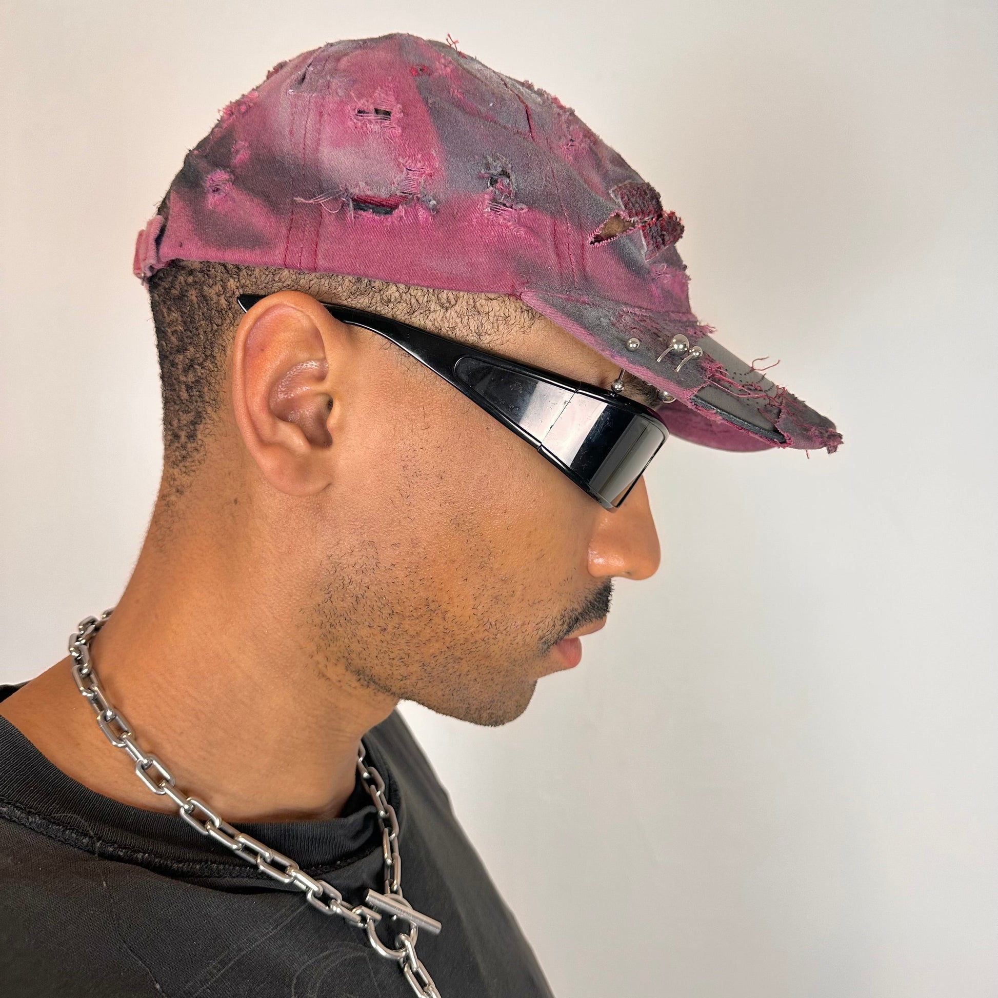 Right side of ASTROBOI* Burn Out red New York hat with distressed finish, white and black paint details, and stainless steel piercings, adjustable back strap.