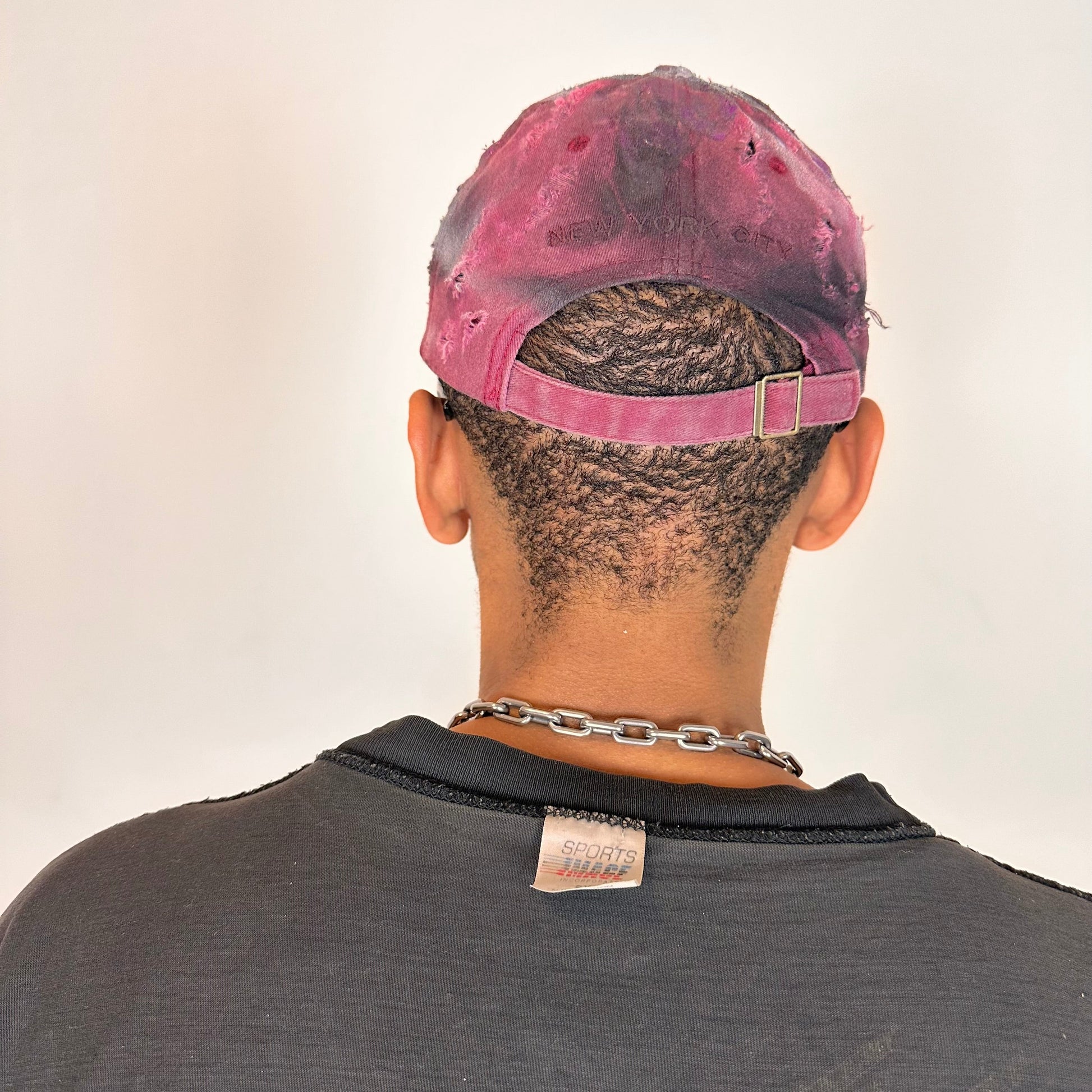 Back of ASTROBOI* Burn Out red New York hat with distressed finish, white and black paint details, and stainless steel piercings, adjustable back strap.