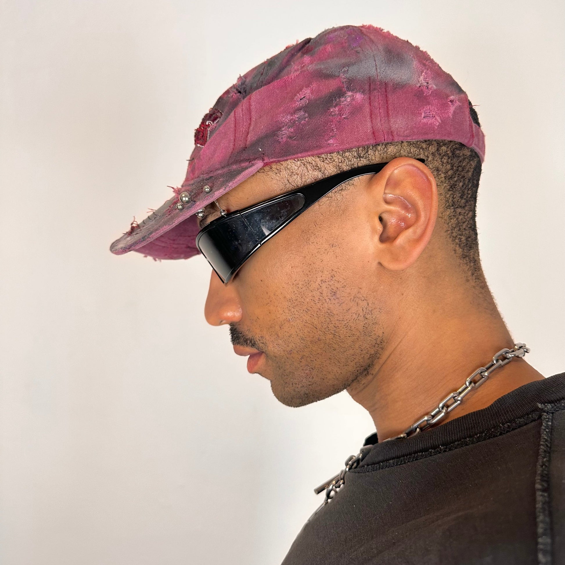 Left of ASTROBOI* Burn Out red New York hat with distressed finish, white and black paint details, and stainless steel piercings, adjustable back strap.