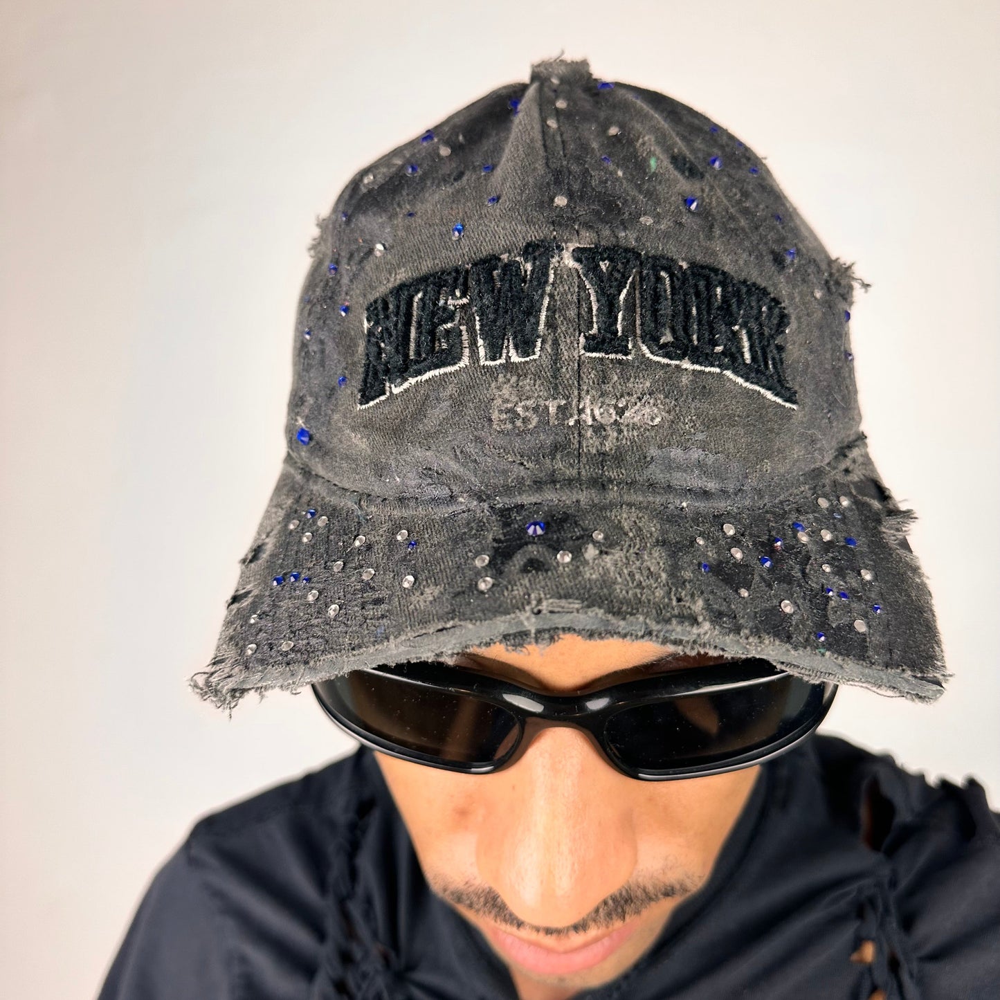 Front of ASTROBOI* New York black distressed half visor hat with rhinestone accents, metallic paint detailing, and raw hem visor edge