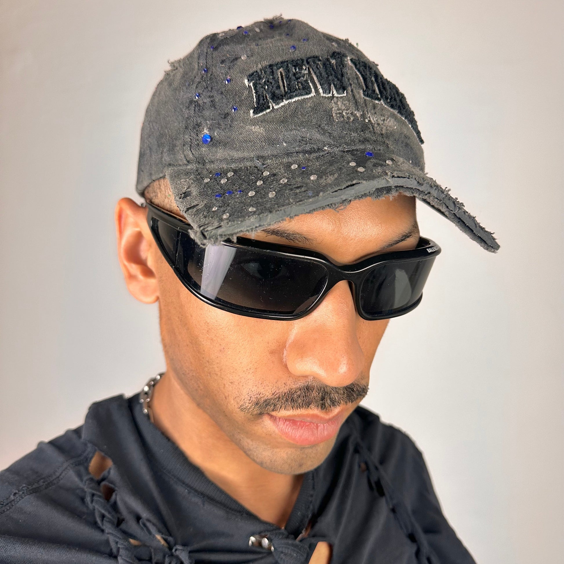 Front right of ASTROBOI* New York black distressed half visor hat with rhinestone accents, metallic paint detailing, and raw hem visor edge