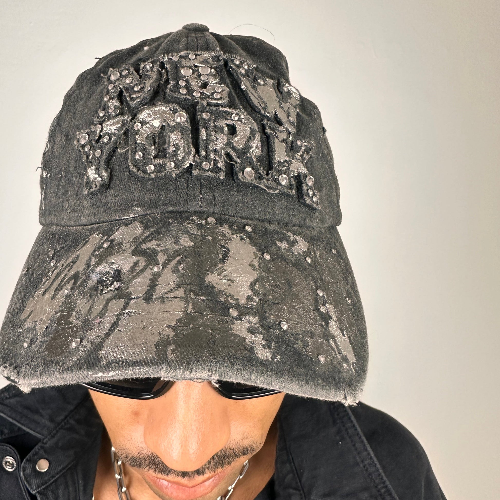 Front of ASTROBOI* chrome New York baseball cap with metallic silver paint, rhinestone logo lettering, distressed finish, and rhinestone visor detailing