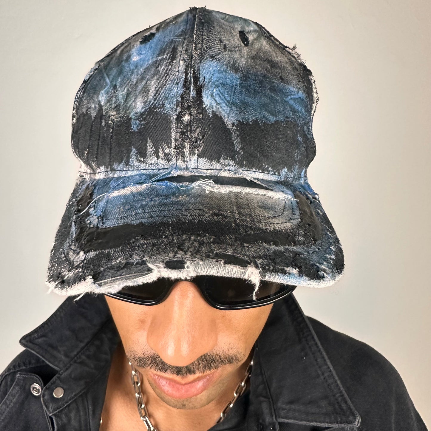 Front of ASTROBOI* white trompe l’oeil denim print hat with blue and black paint, resin accents, and distressed detailing.