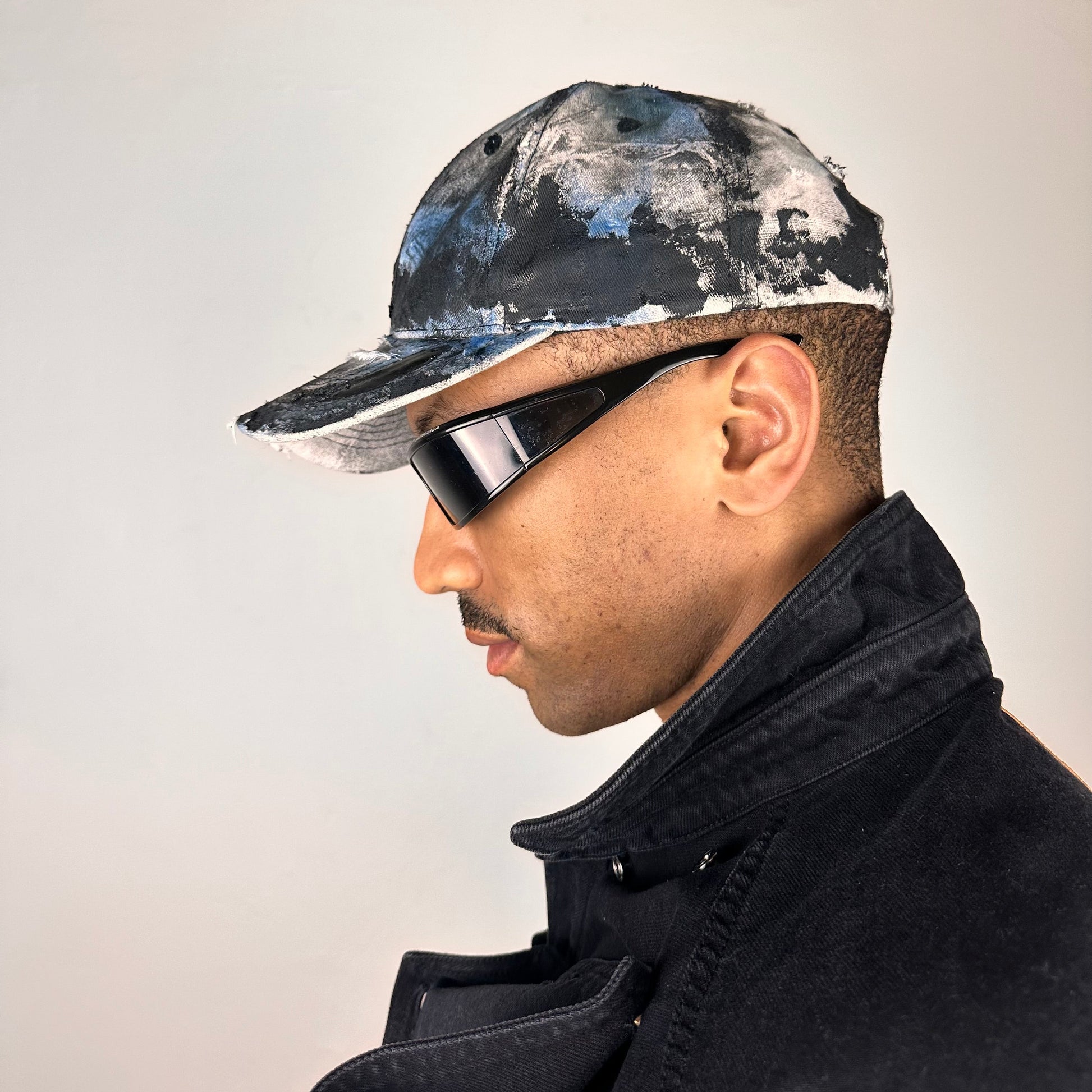 Left side of ASTROBOI* white trompe l’oeil denim print hat with blue and black paint, resin accents, and distressed detailing.