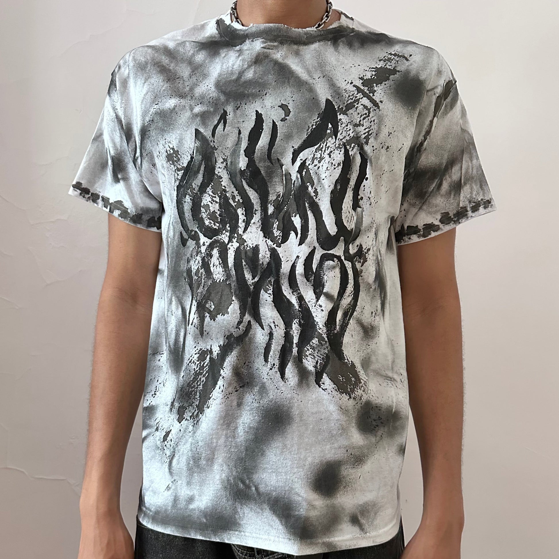 Close-up of ASTROBOI* x Gildan 'Slither' showing impressionist black flame chest design and black and gray hazy splatter detailing on white cotton fabric.