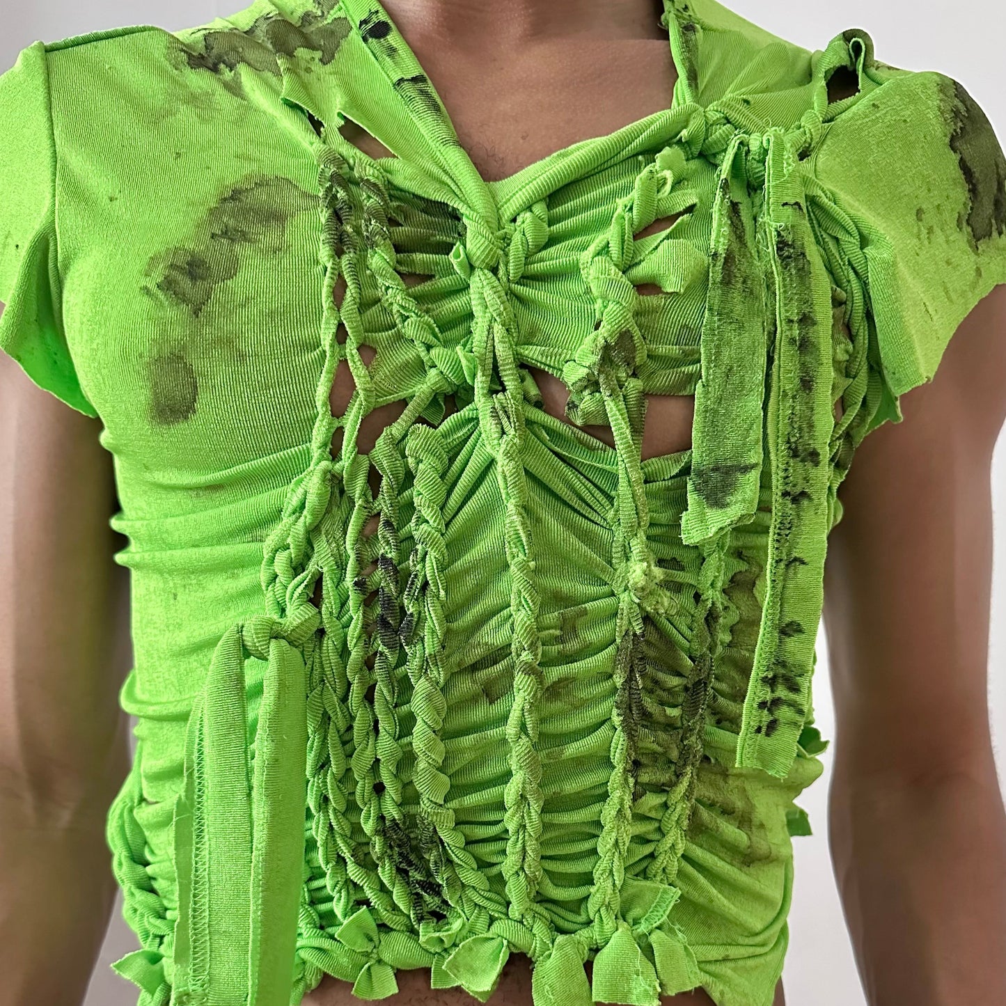 Close-up of ASTROBOI* 'SS26' showing hand-braided construction and black watercolor paint detail on neon green stretch fabric.
