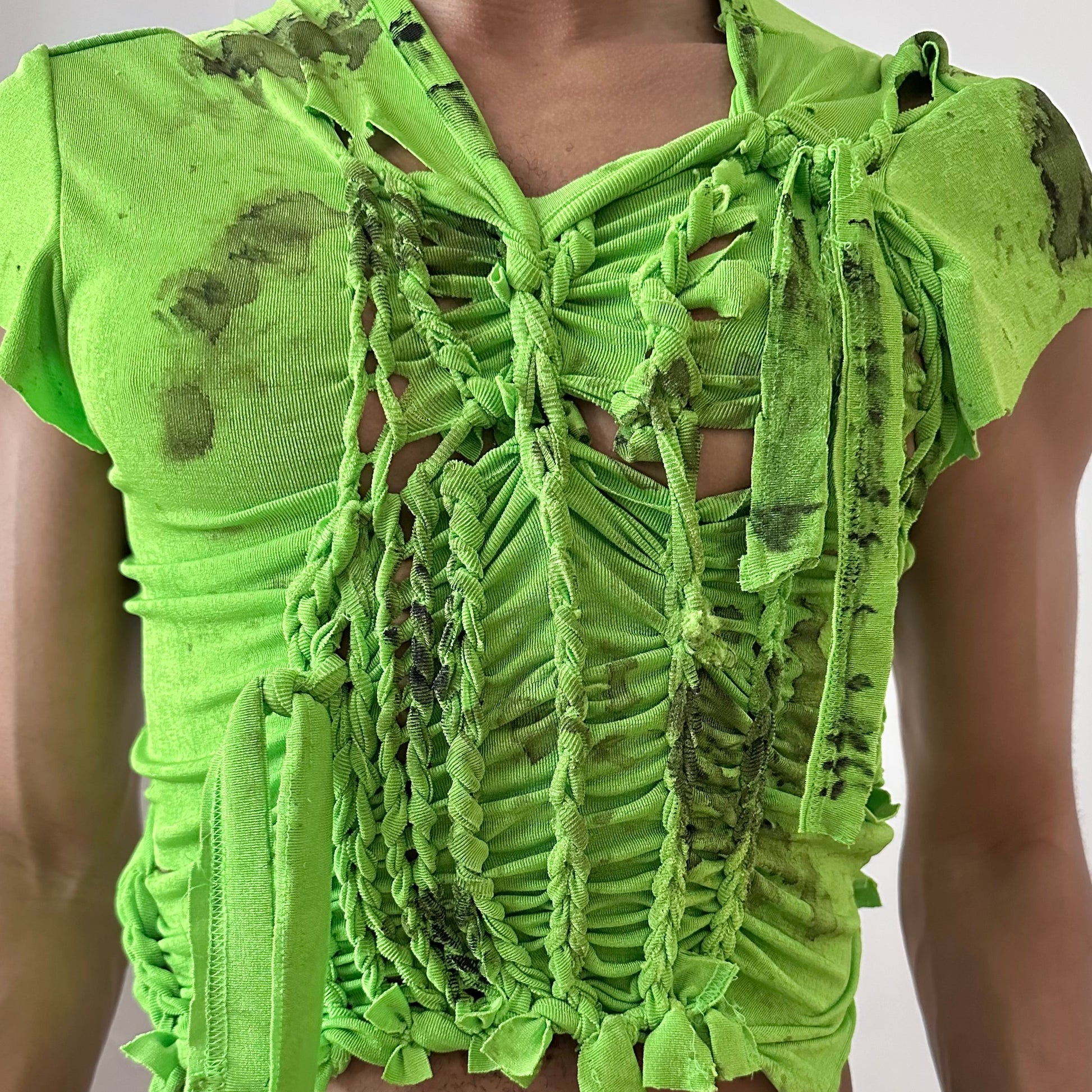 Close-up of ASTROBOI* 'SS26' showing hand-braided construction and black watercolor paint detail on neon green stretch fabric.