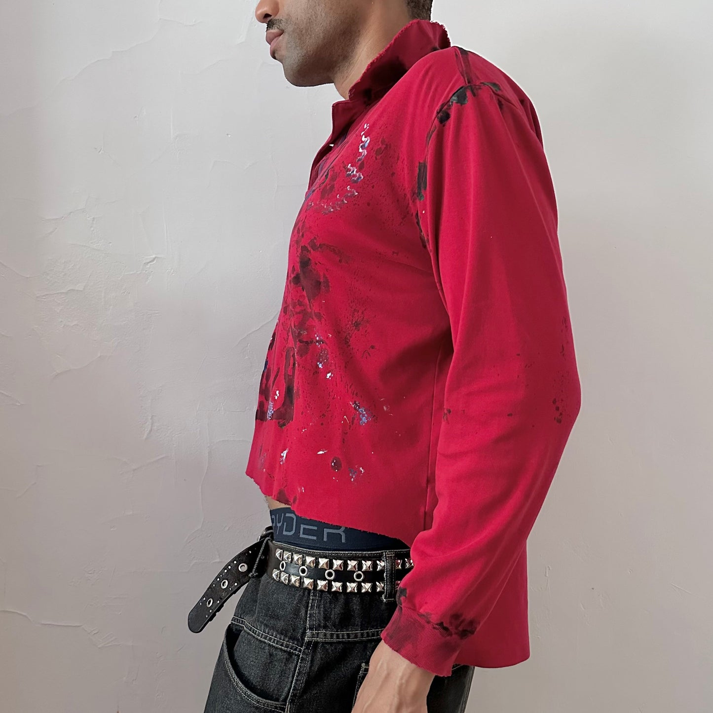 Left side detail of ASTROBOI* x Polo Ralph Lauren 'Kill Switch' showing hand-painted black, blue, and white expressionist pattern and side slit detail on red polo.