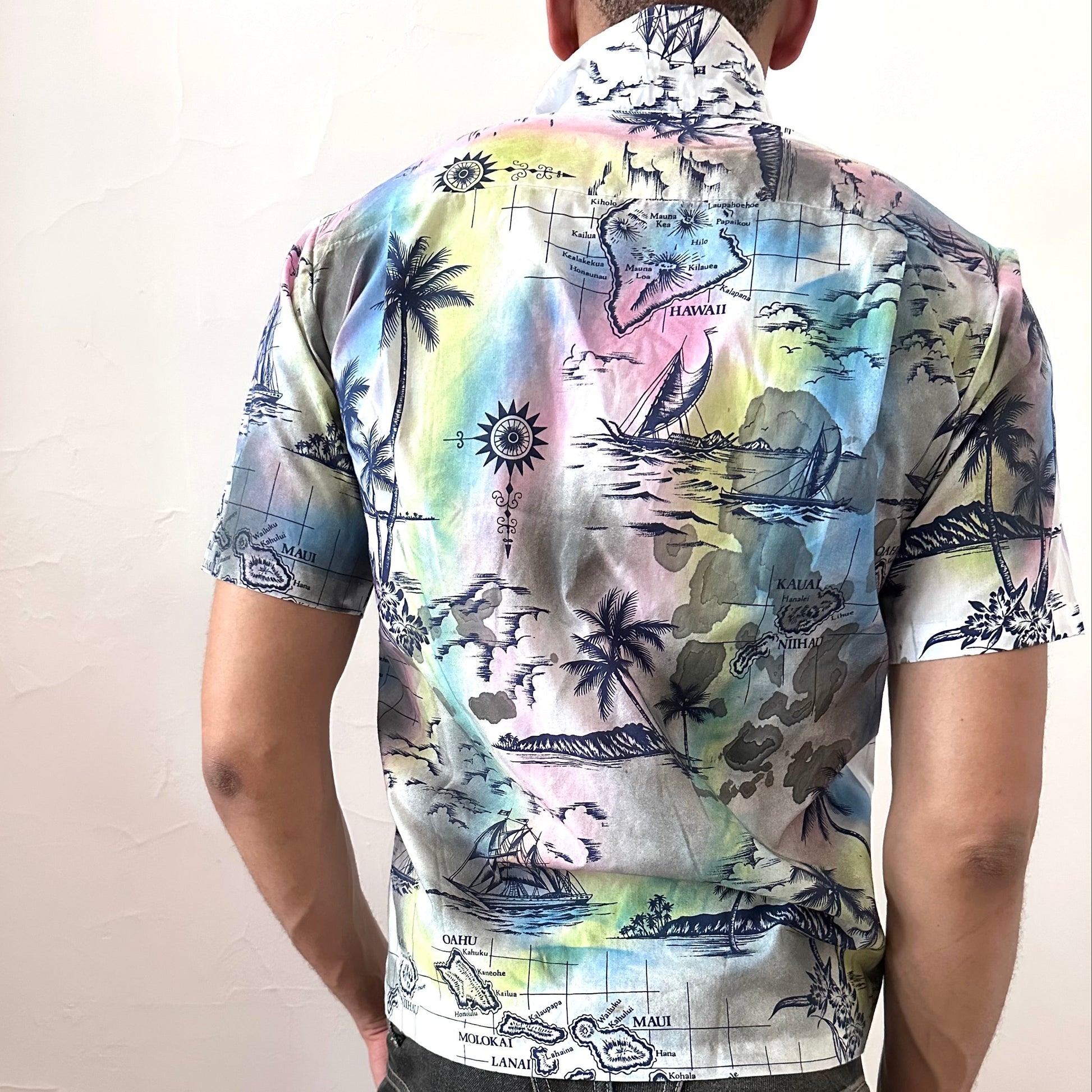 ASTROBOI* 'Sulfur Surfer' white tropical graphic button up shirt, rear view showing navy Hawaiian iconography paint treatment, worn by male model.
