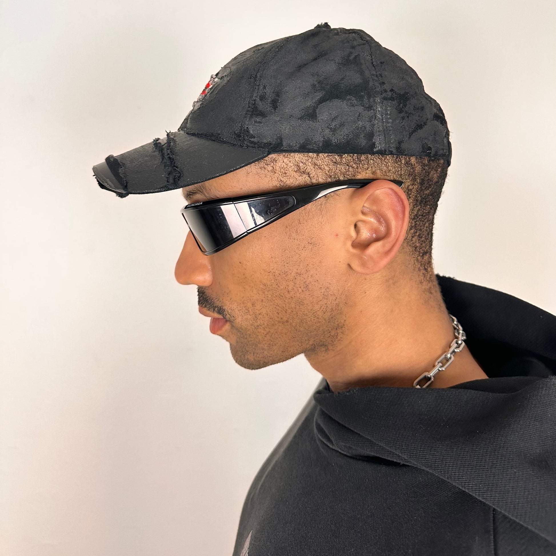 Left side of ASTROBOI* x Chevy black distressed baseball hat with resin-sealed rhinestone logo, deconstructed visor, wax-painted tattoo details, adjustable fit