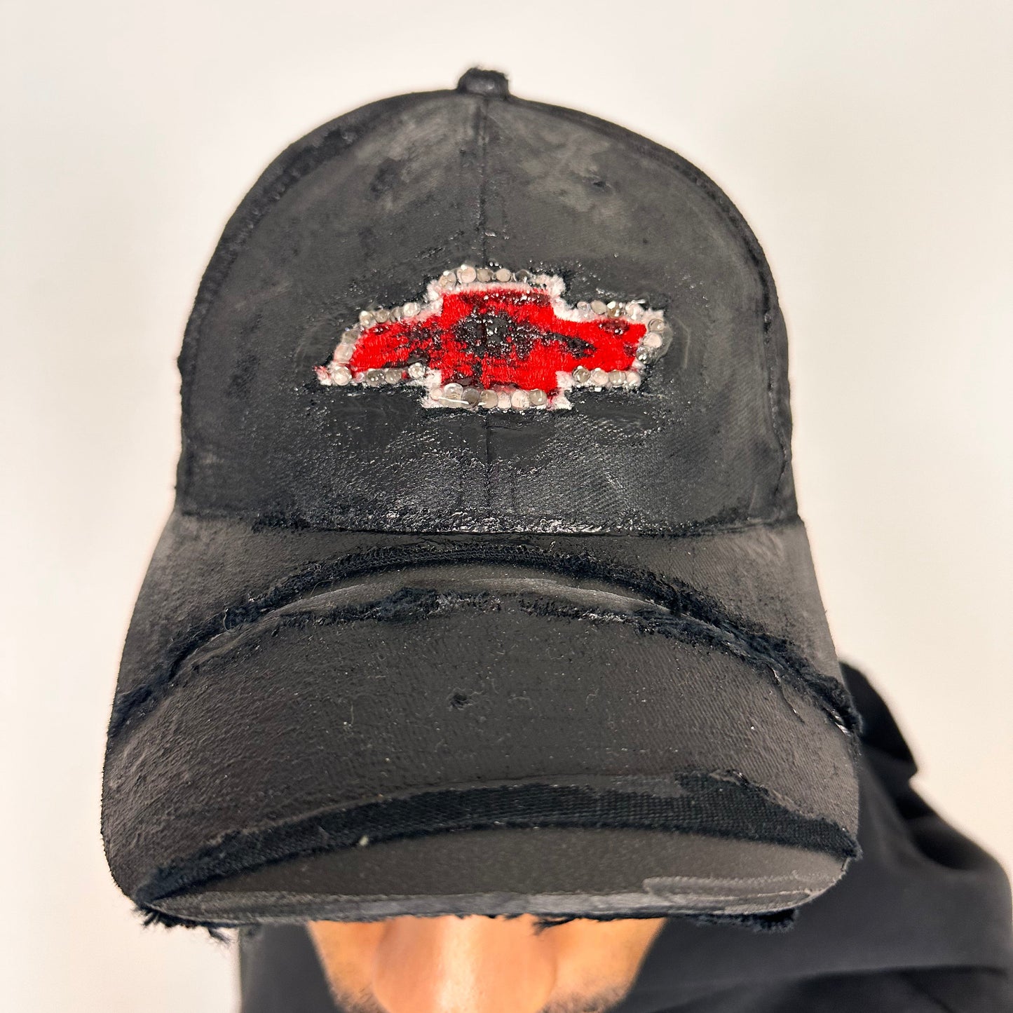Front of ASTROBOI* x Chevy black distressed baseball hat with resin-sealed rhinestone logo, deconstructed visor, wax-painted tattoo details, adjustable fit