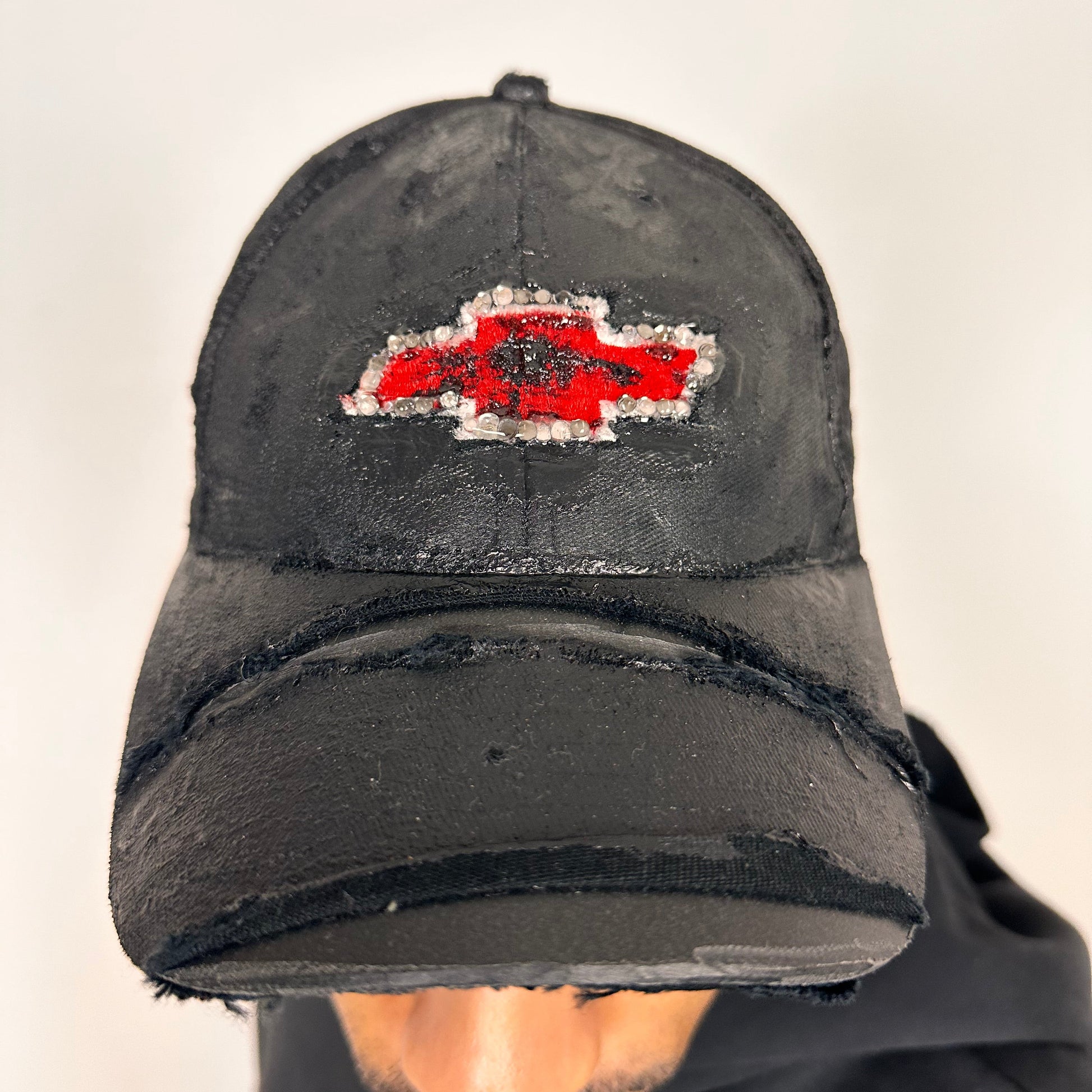 Front of ASTROBOI* x Chevy black distressed baseball hat with resin-sealed rhinestone logo, deconstructed visor, wax-painted tattoo details, adjustable fit