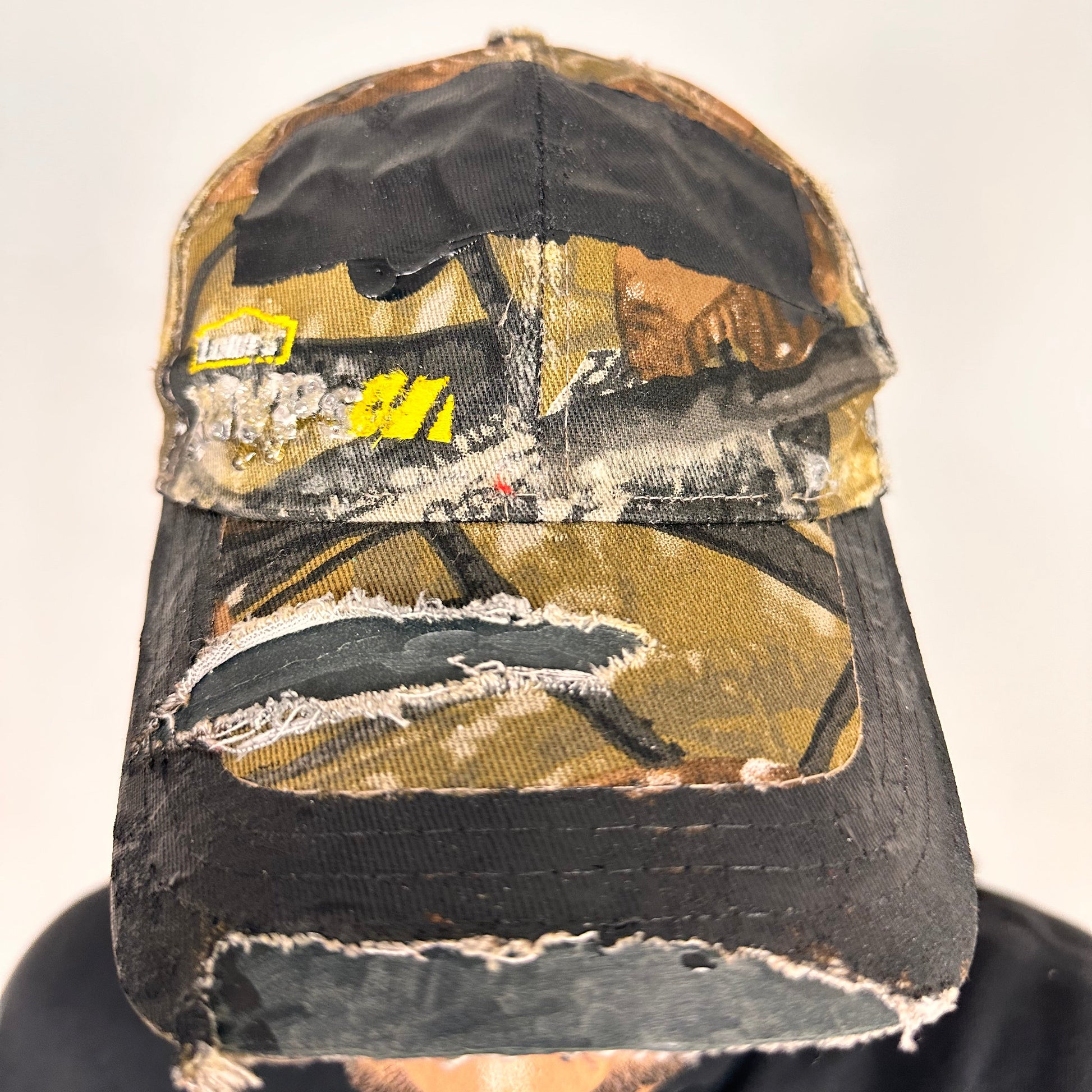 Front of ASTROBOI* x Lowe’s MVP brown RealTree camouflage hat with resin-sealed rhinestone logo, black waxed tattoo print, adjustable strap, custom NYC piece