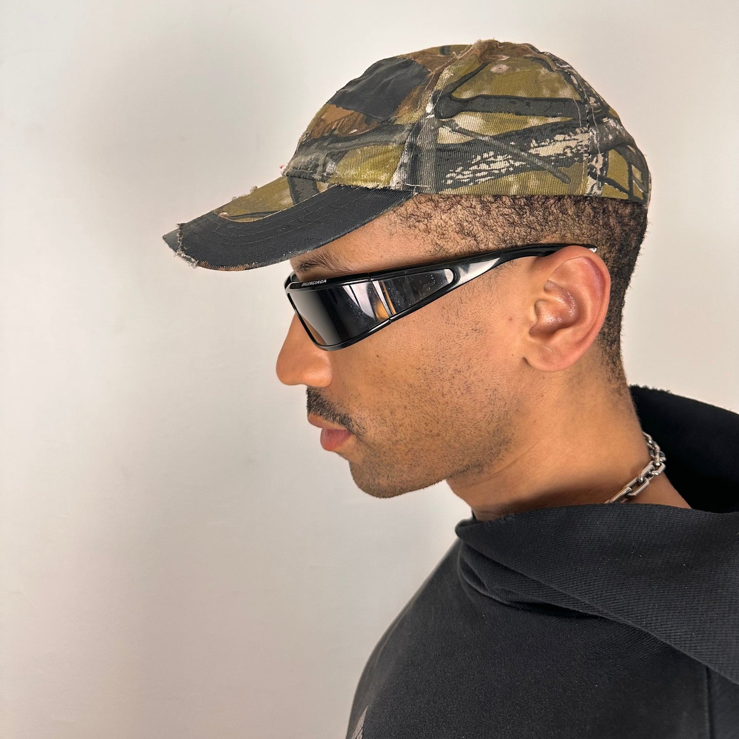 Left side on ASTROBOI* x Lowe’s MVP brown RealTree camouflage hat with resin-sealed rhinestone logo, black waxed tattoo print, adjustable strap, custom NYC piece