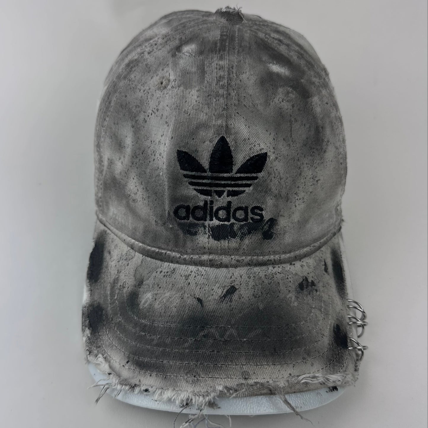Close-up of ASTROBOI* x Adidas 'H Chic' showing Adidas logo, black paint detailing, distressed finish, and stainless steel piercing detail on tan base.