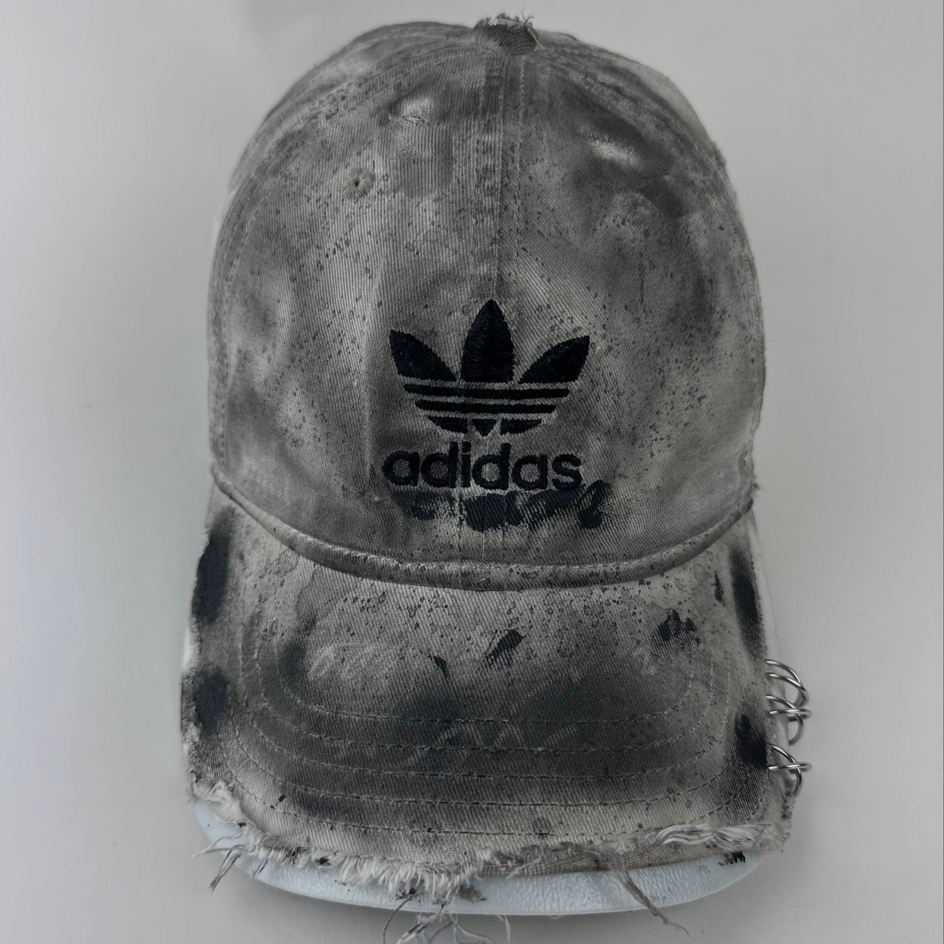 Close-up of ASTROBOI* x Adidas 'H Chic' showing Adidas logo, black paint detailing, distressed finish, and stainless steel piercing detail on tan base.