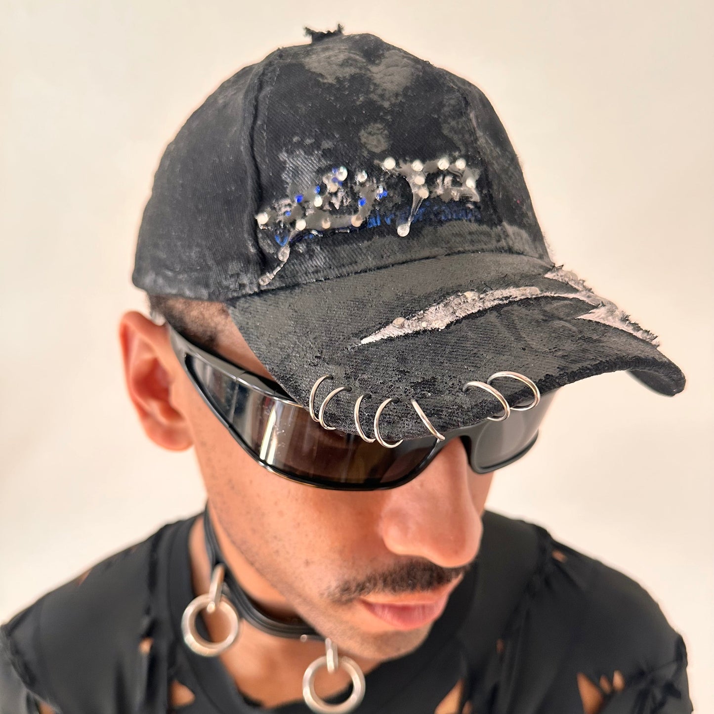 Piercing details on ASTROBOI* Speed Racing black and white checkered utility hat with resin-set rhinestones, stainless steel piercings, and hand-painted detailing